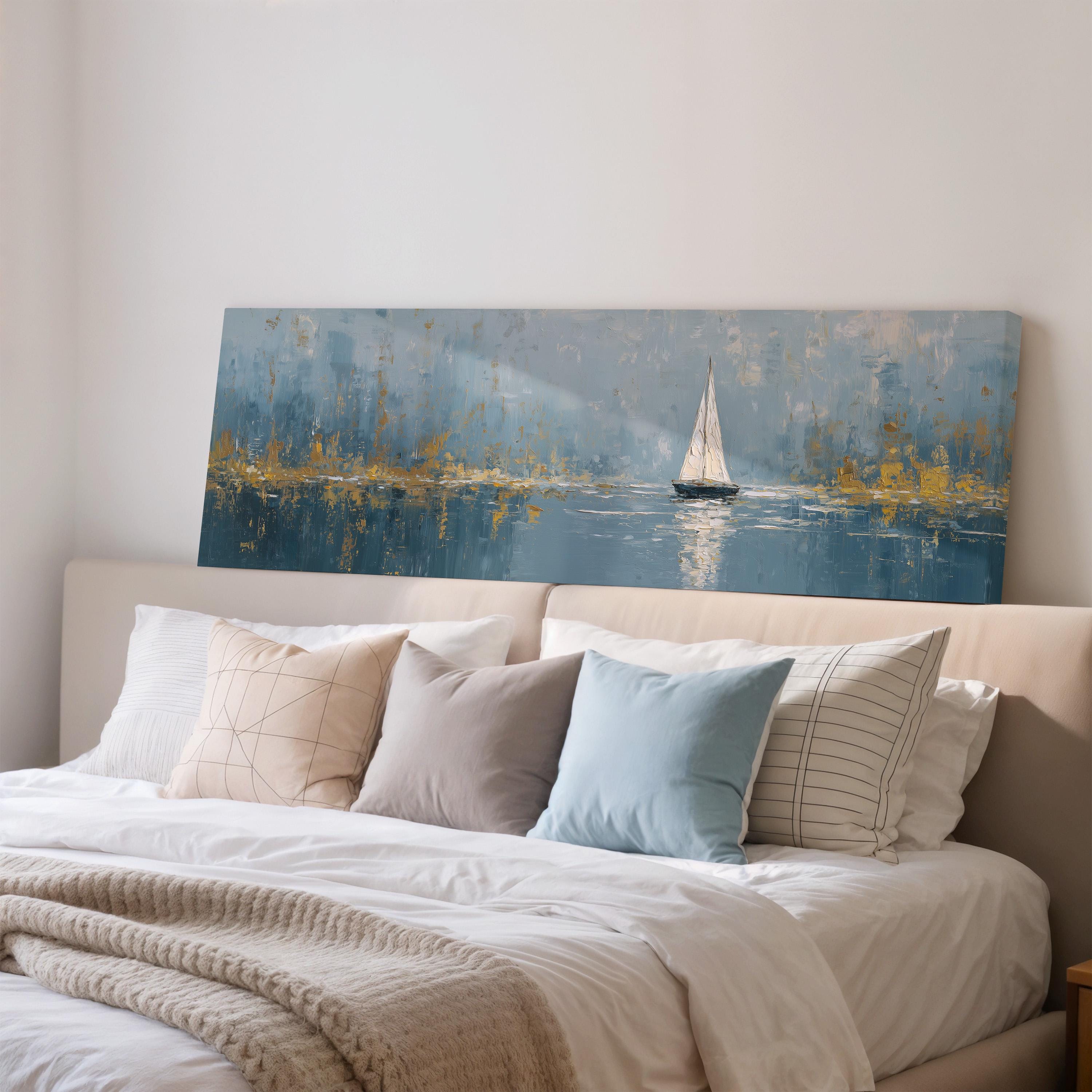 a large painting of a sailboat on a body of water, hanging on a wall above a bed with white pillows and a gray blanket.