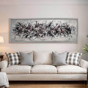 a large, abstract painting hanging on a wall above a white couch with gray and white patterned pillows.