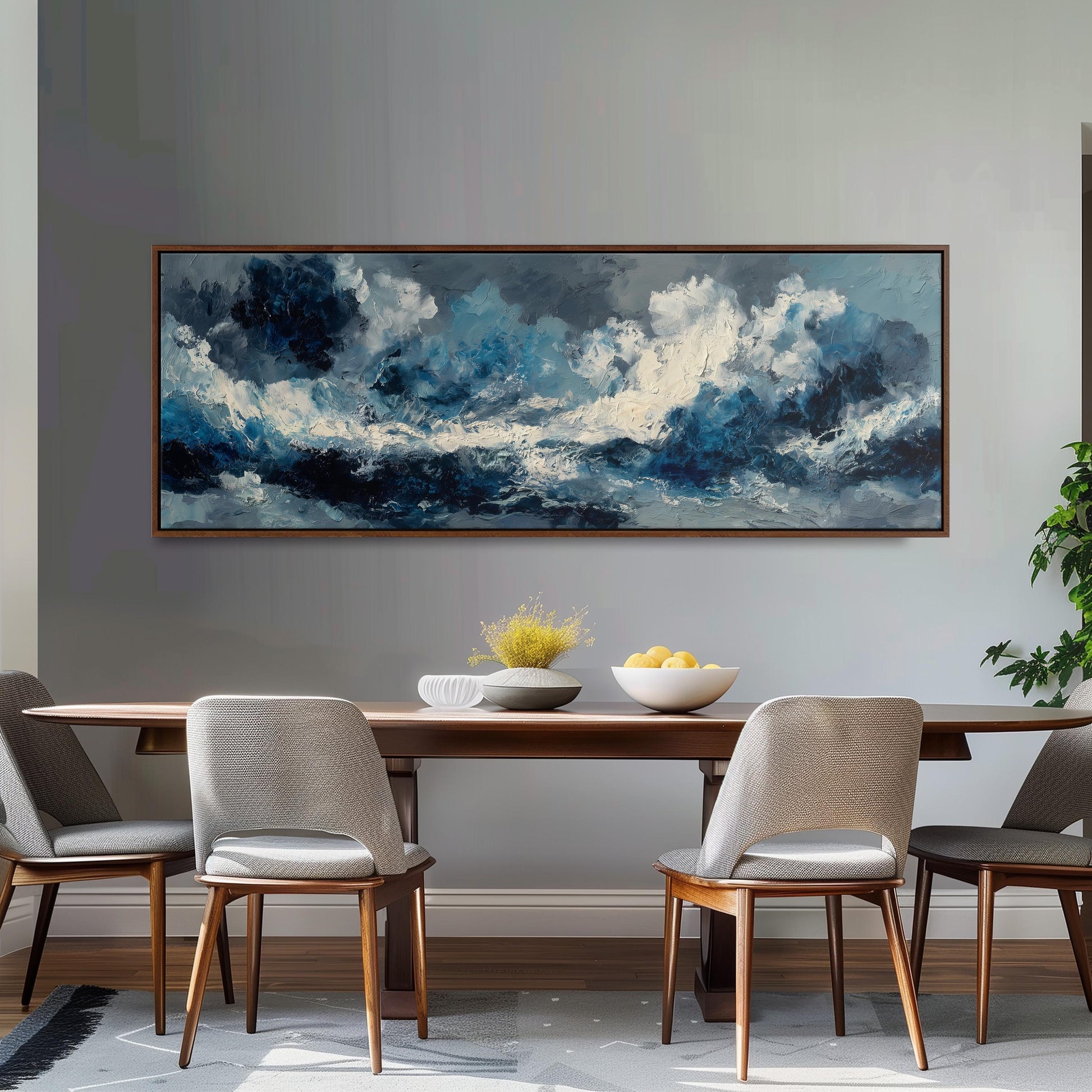 a large painting of a stormy sea hanging on a wall above a wooden dining table with four chairs. The table is set with a bowl of fruit and a vase of flowers, creating a cozy and inviting atmosphere.