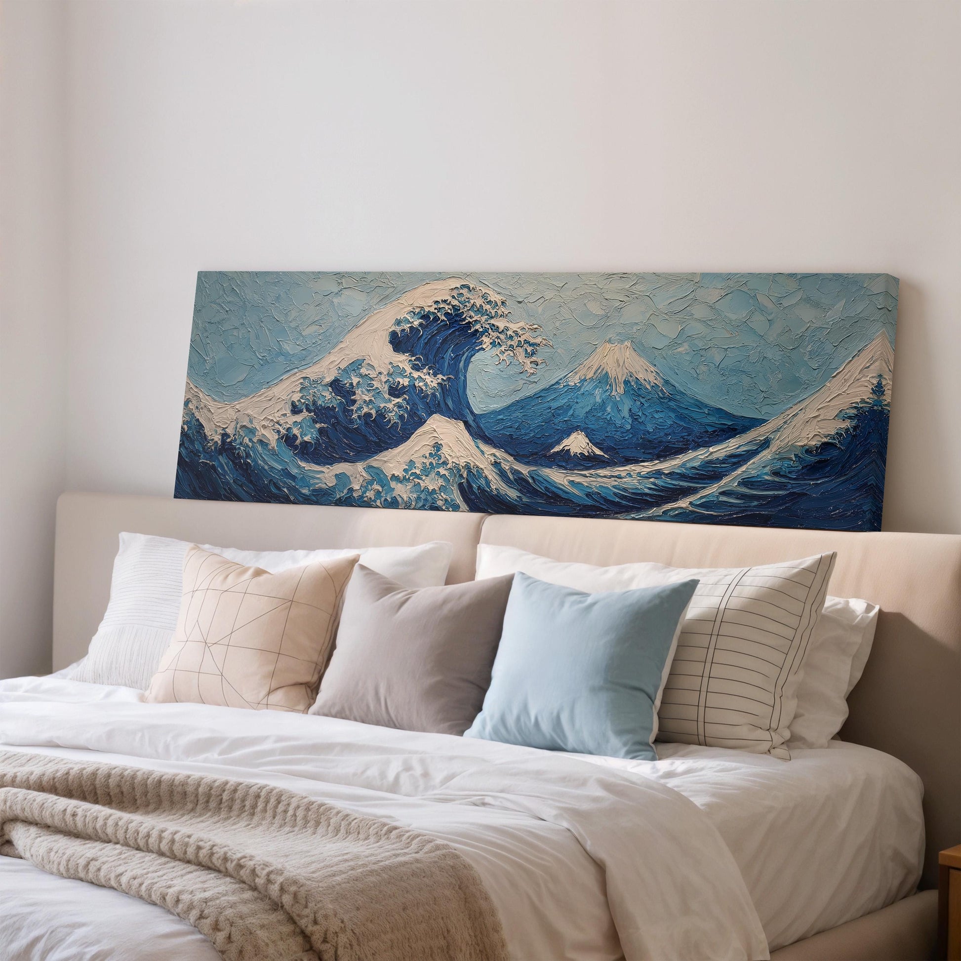 a large, framed painting of a wave above a bed with white pillows and a gray blanket.