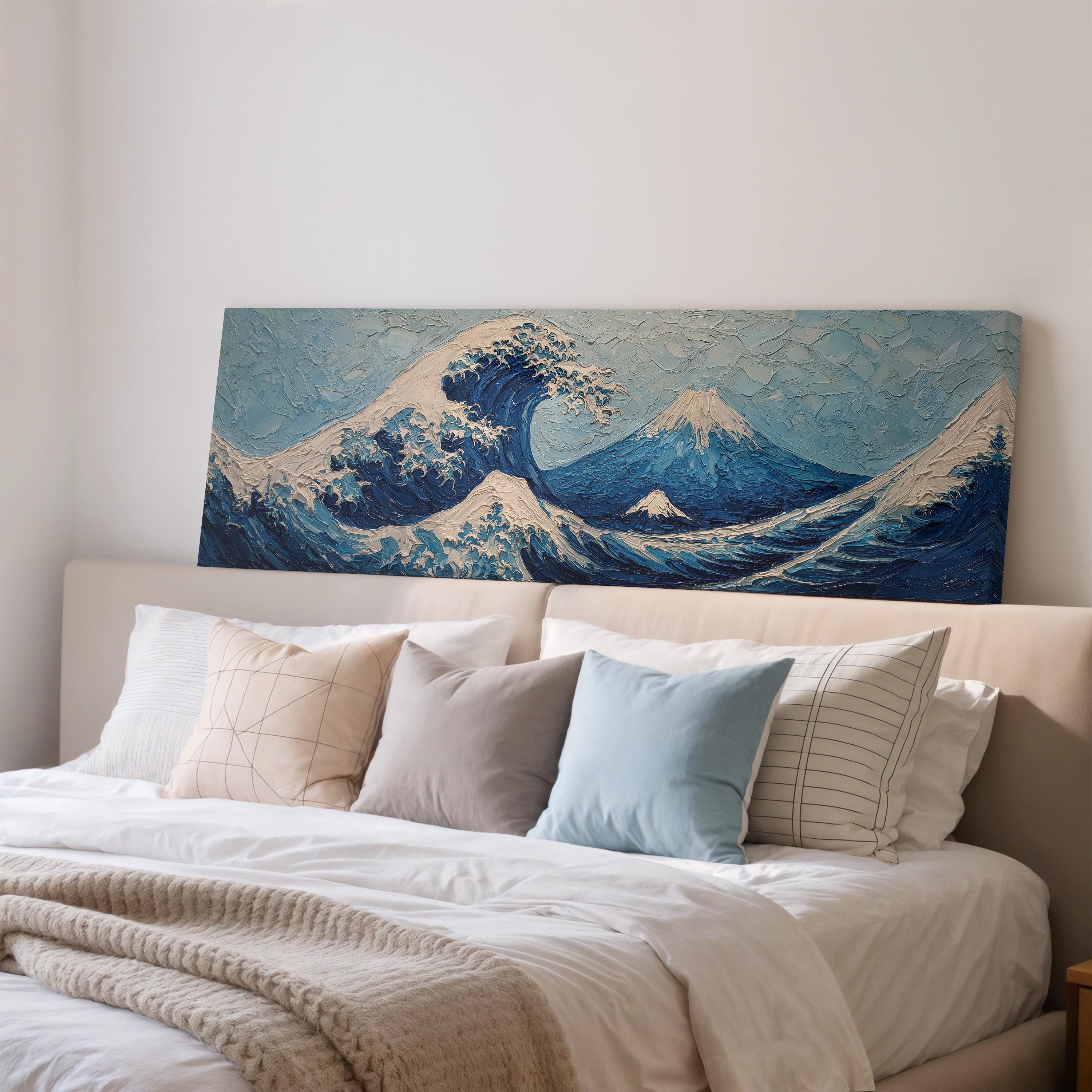a large, framed painting of a wave above a bed with white pillows and a gray blanket.