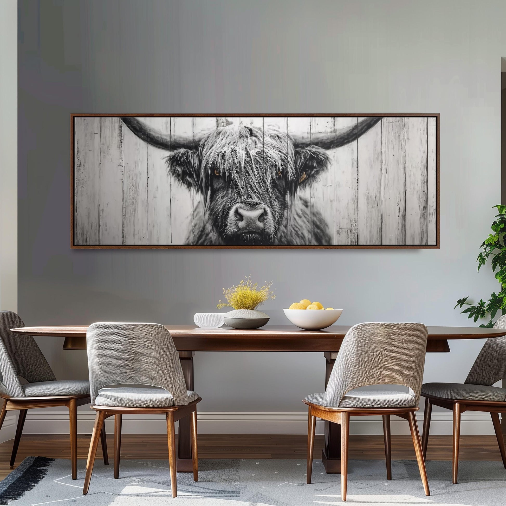 a dining room with a large framed picture of a cow's head hanging on the wall above a wooden dining table with four chairs.