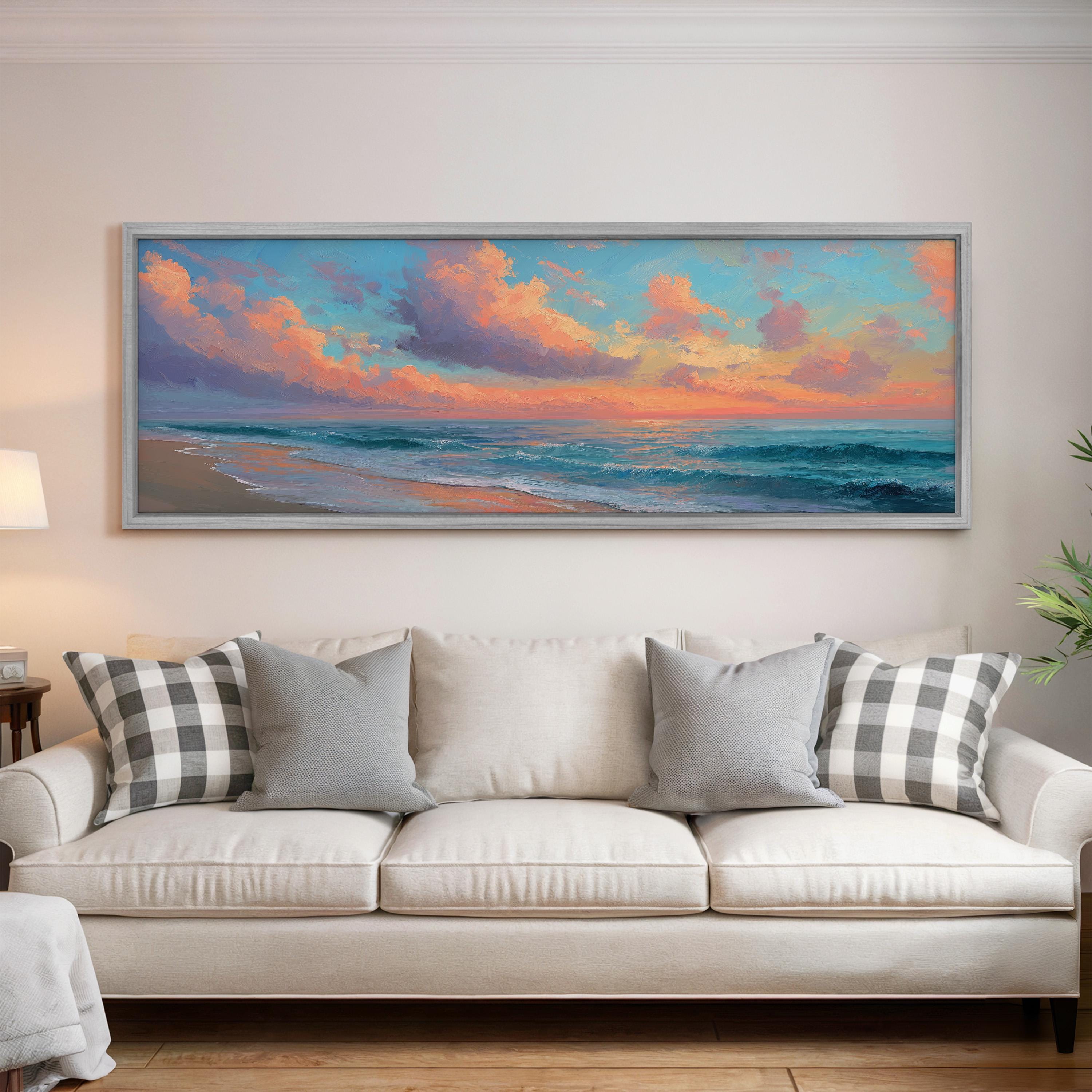 a large, framed painting of a beach scene hanging on a wall above a white couch with gray and white plaid throw pillows.