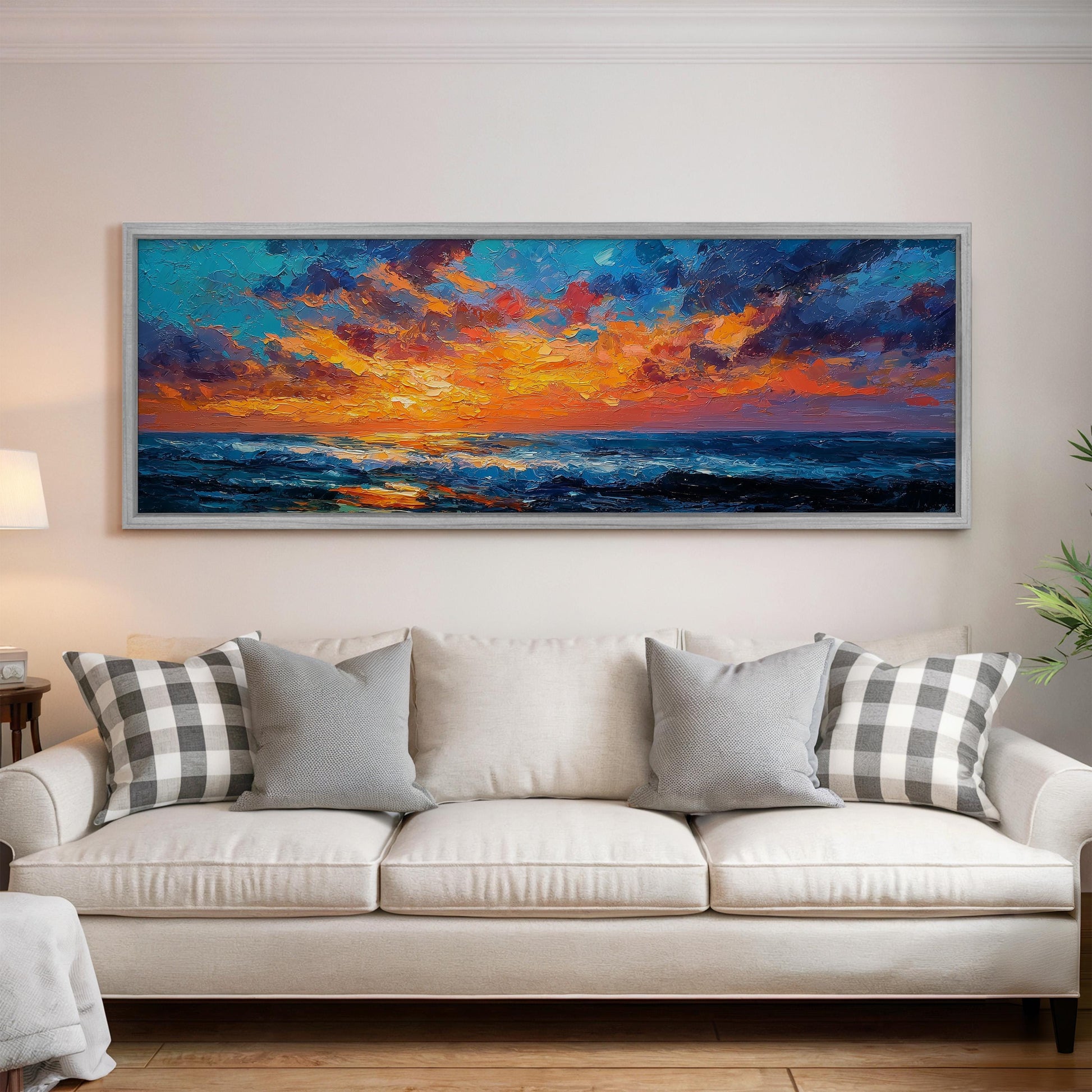 a large, colorful painting of a sunset over the ocean hanging on a wall above a white couch with gray and white patterned pillows.