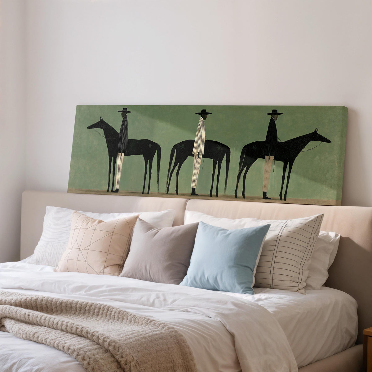 Three stylized cowboys with horses on sage green wide panoramic canvas print above a bed in a bedroom