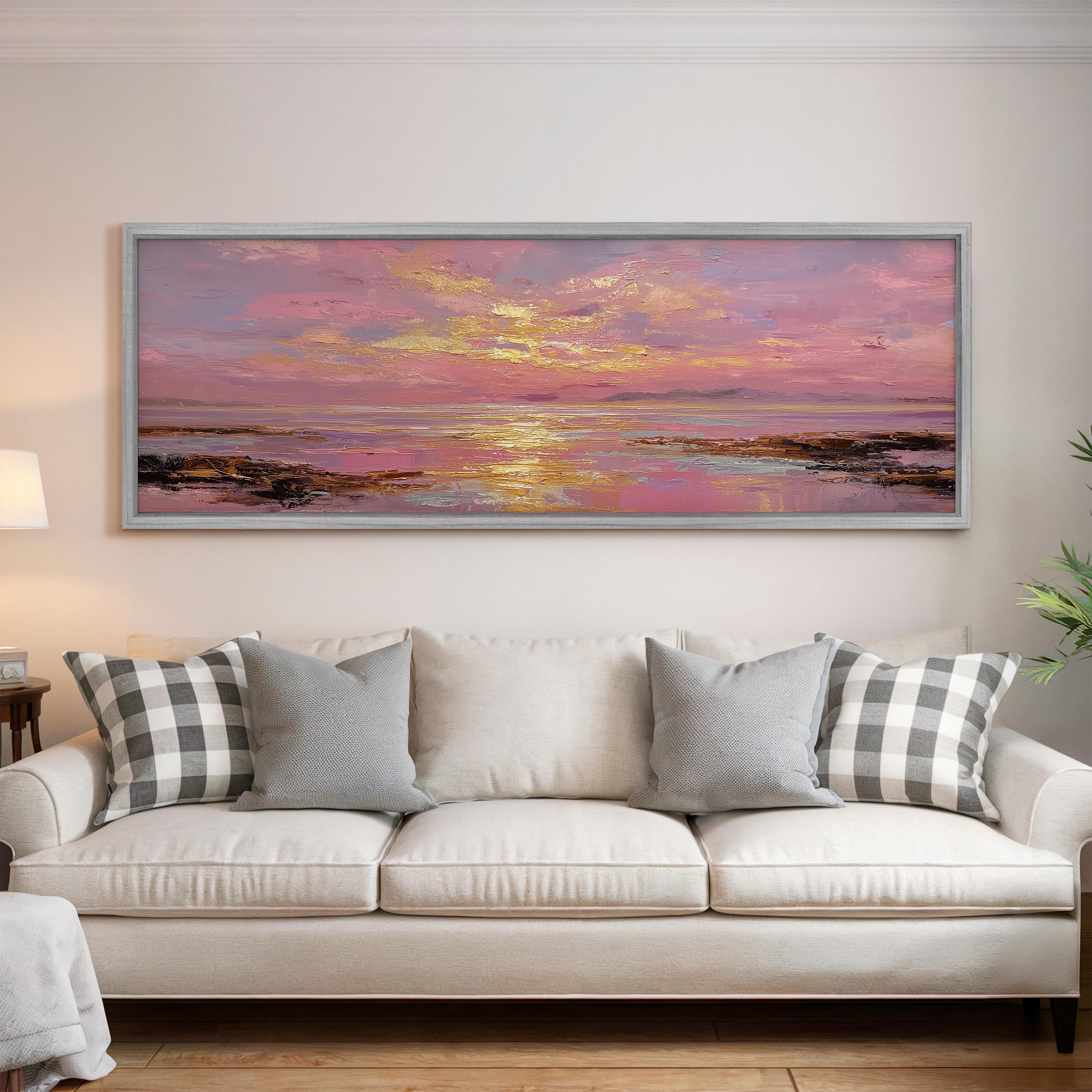 a large, framed painting of a sunset over a body of water, hanging on a wall above a white sofa with patterned throw pillows.