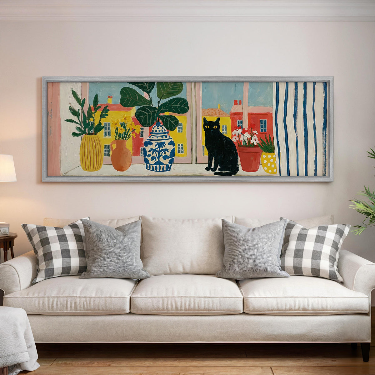 Black cat on a windowsill overlooking a colorful village panoramic canvas print above a white sofa in a bright living room
