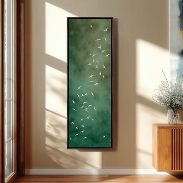 a large framed painting of white birds against a green background, hanging on a wall in a room with a wooden cabinet and a vase of flowers.