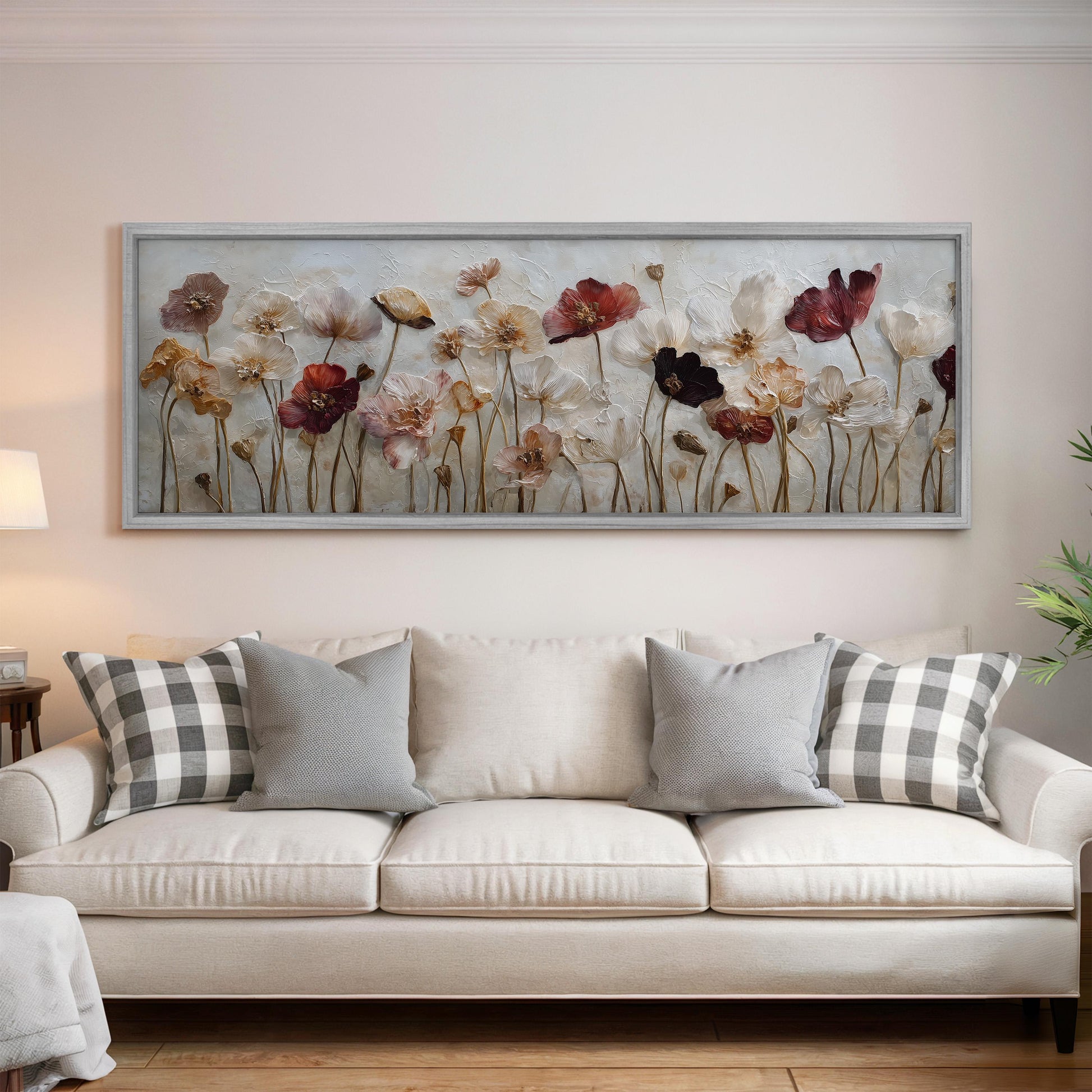 a large framed painting of flowers hanging on a wall above a white couch with gray and white pillows.