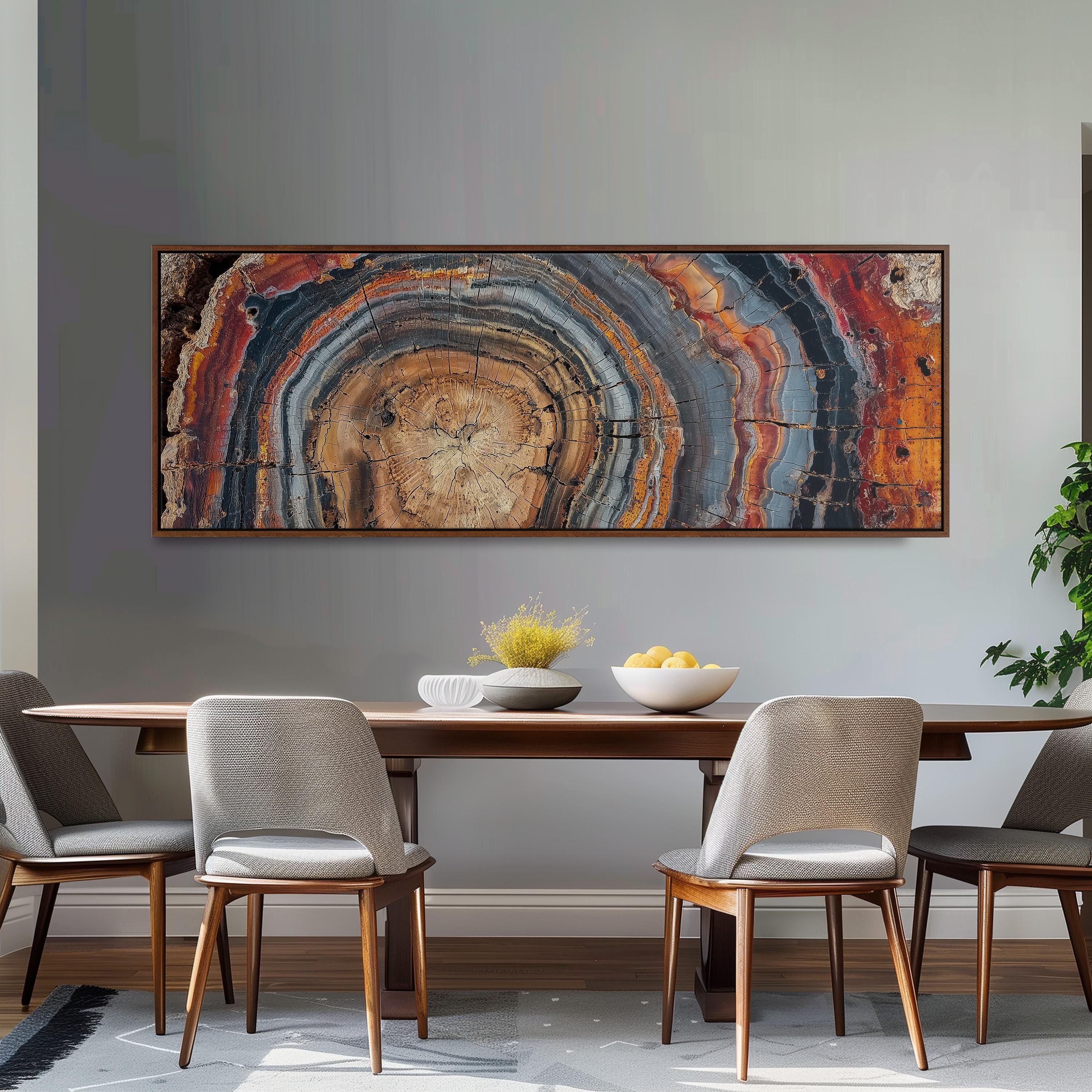 a dining room with a wooden table and four chairs. Above the table, there is a large abstract painting with a colorful, striped design. On the table, there is a bowl of fruit and a vase of flowers.