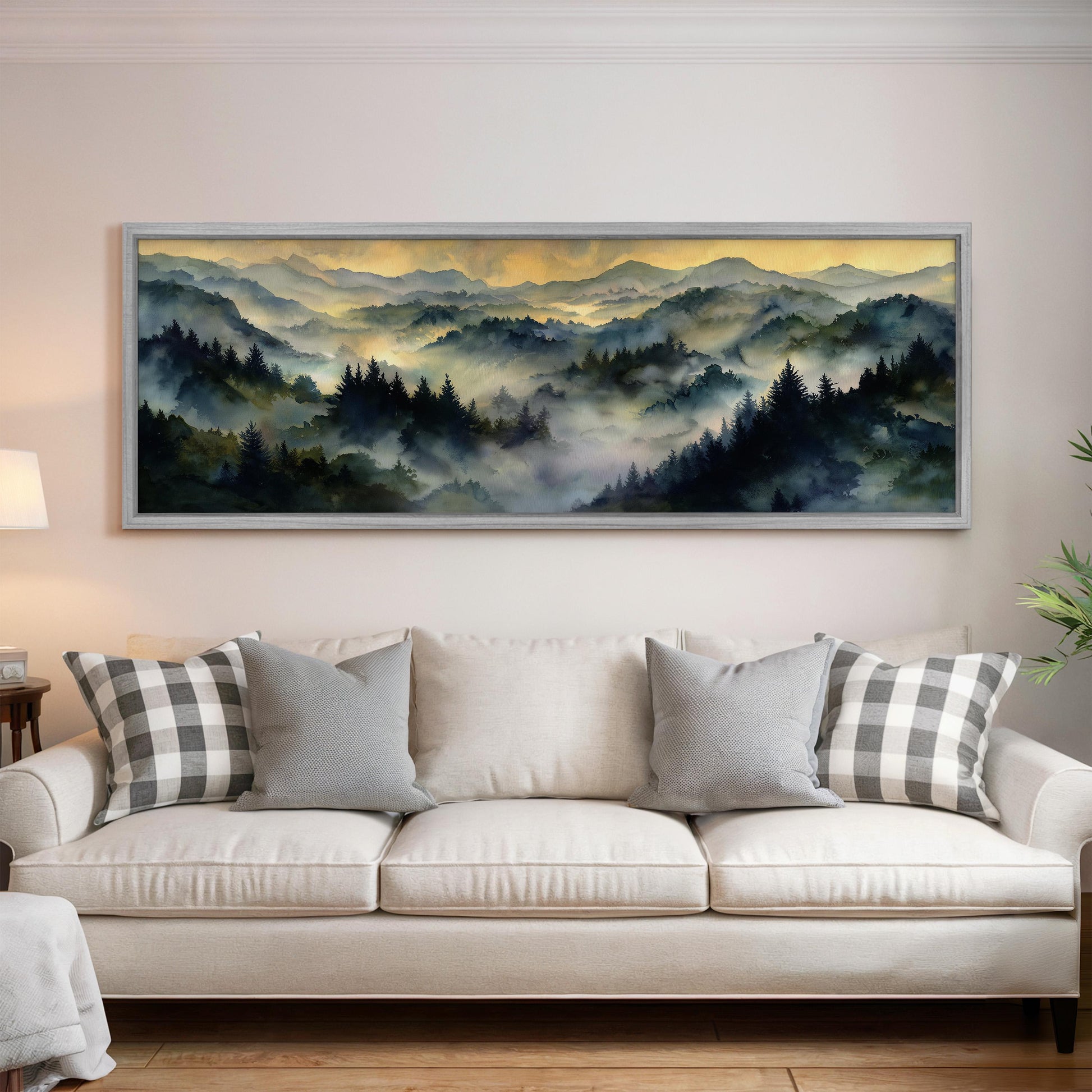 a large, framed painting of a mountainous landscape hanging on a wall above a white couch with gray and white plaid throw pillows.