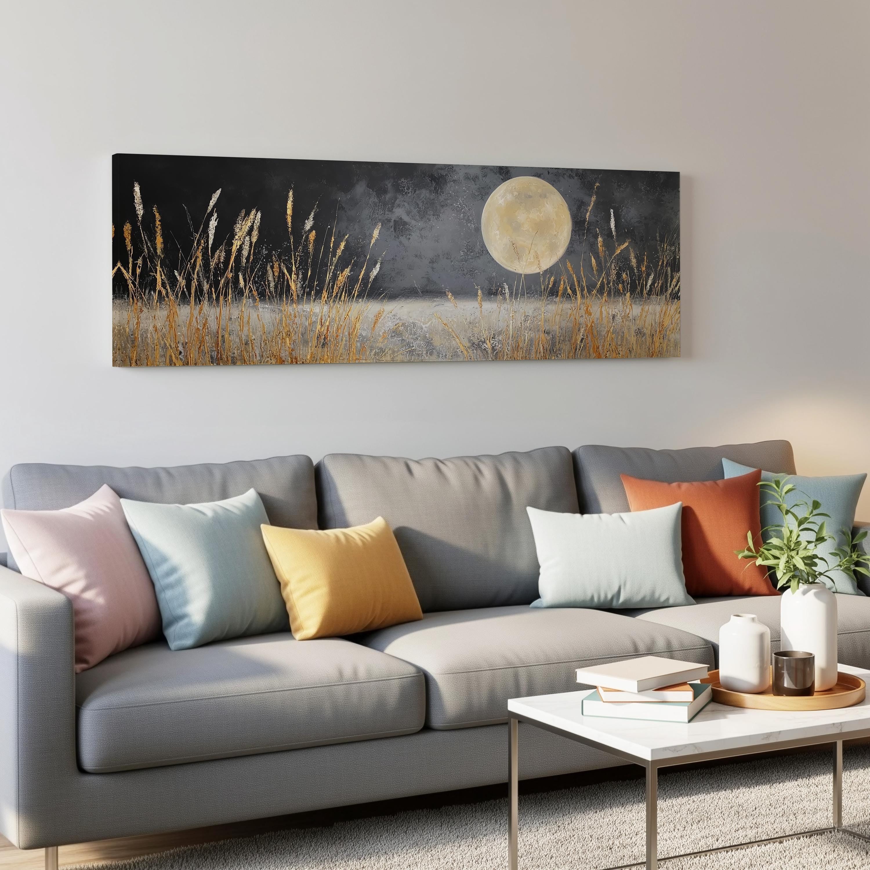 a living room with a gray sofa adorned with colorful throw pillows, a coffee table, and a painting of a field with tall grass and a full moon hanging on the wall above the sofa.