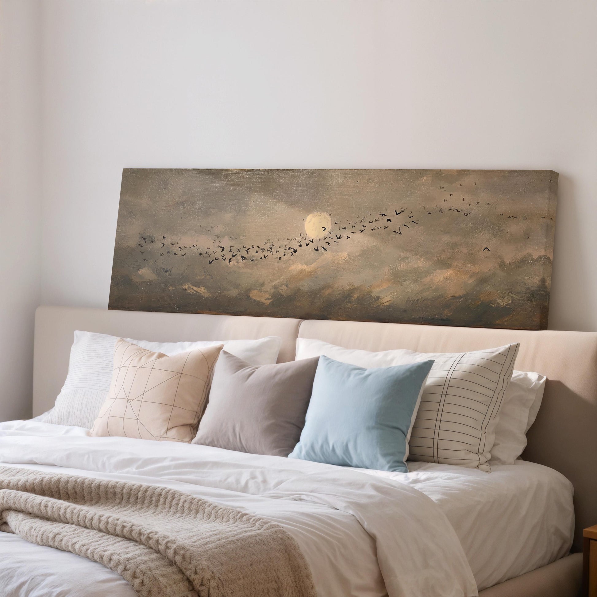 a serene bedroom scene with a large bed adorned with white linens and a variety of colorful pillows. Above the bed, a painting of a flock of birds flying across a cloudy sky is displayed on the wall.