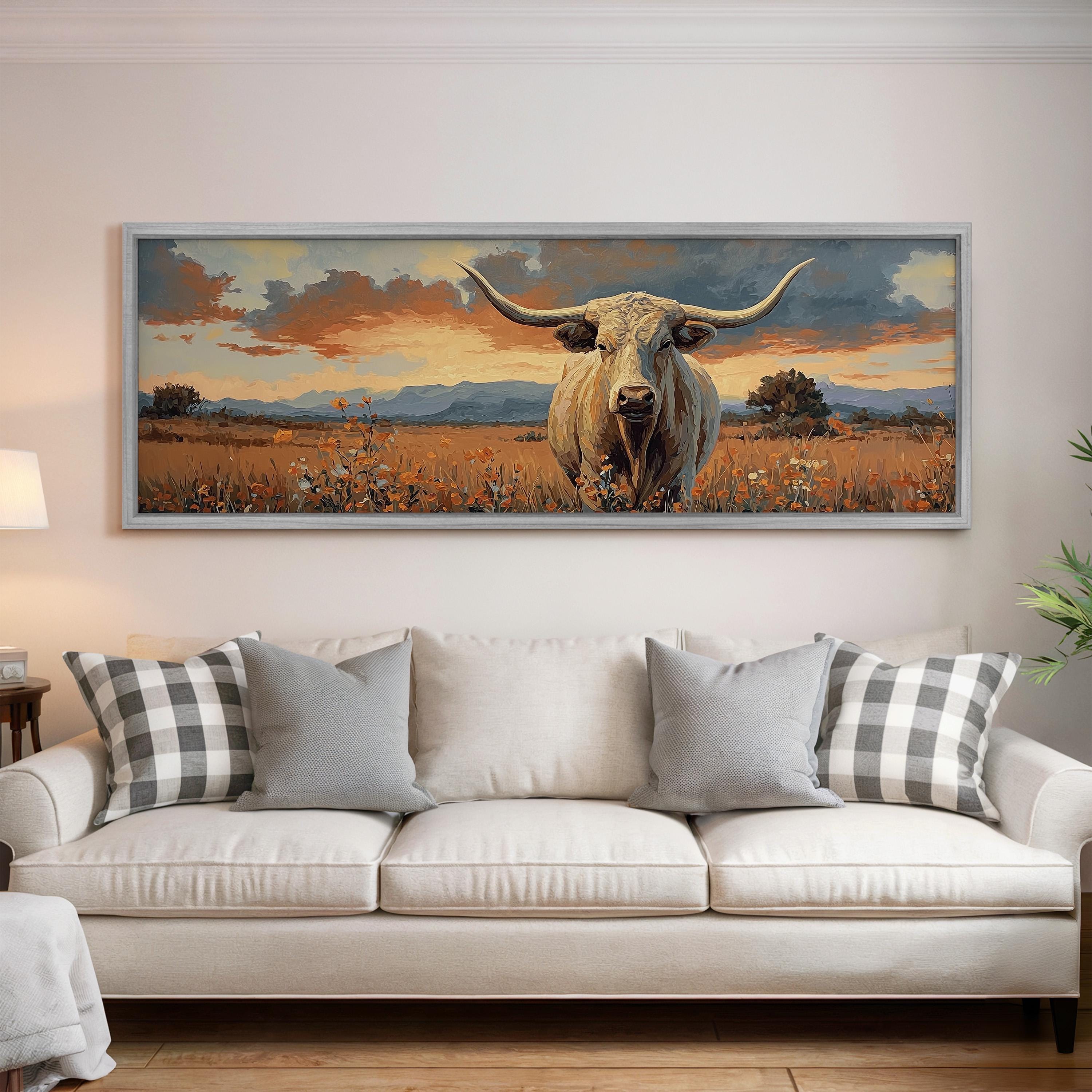 a large painting of a bull with long horns, displayed on a wall above a white couch with plaid throw pillows.