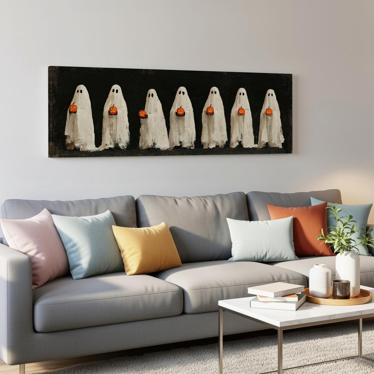 Row of ghosts holding pumpkins panoramic canvas print above a grey sofa in a living room