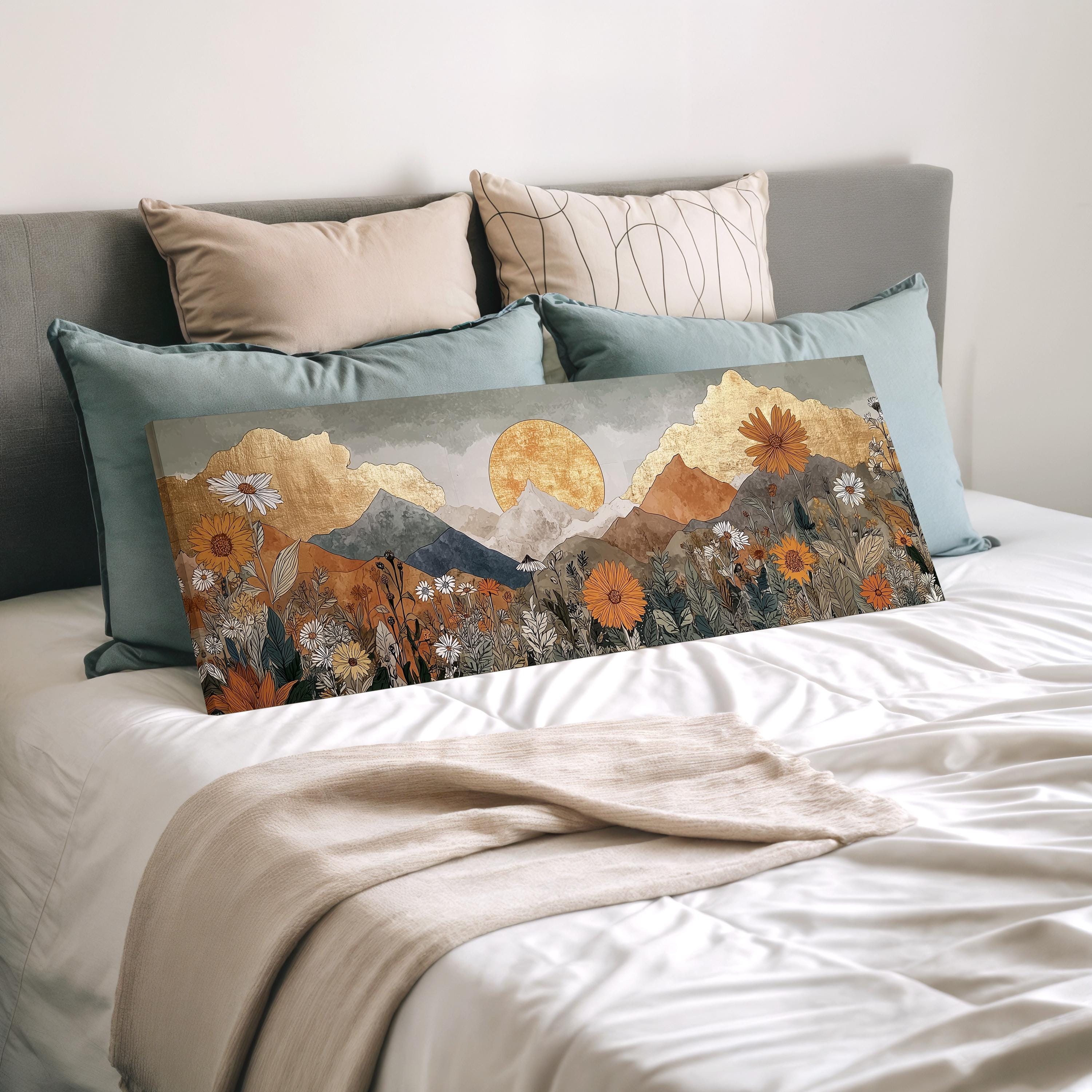 a large canvas print of a mountain landscape with a sun in the sky, placed on a bed with pillows.