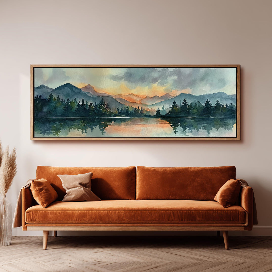 a large, framed painting of a serene landscape with mountains, trees, and a lake, hanging on a wall above a brown sofa.