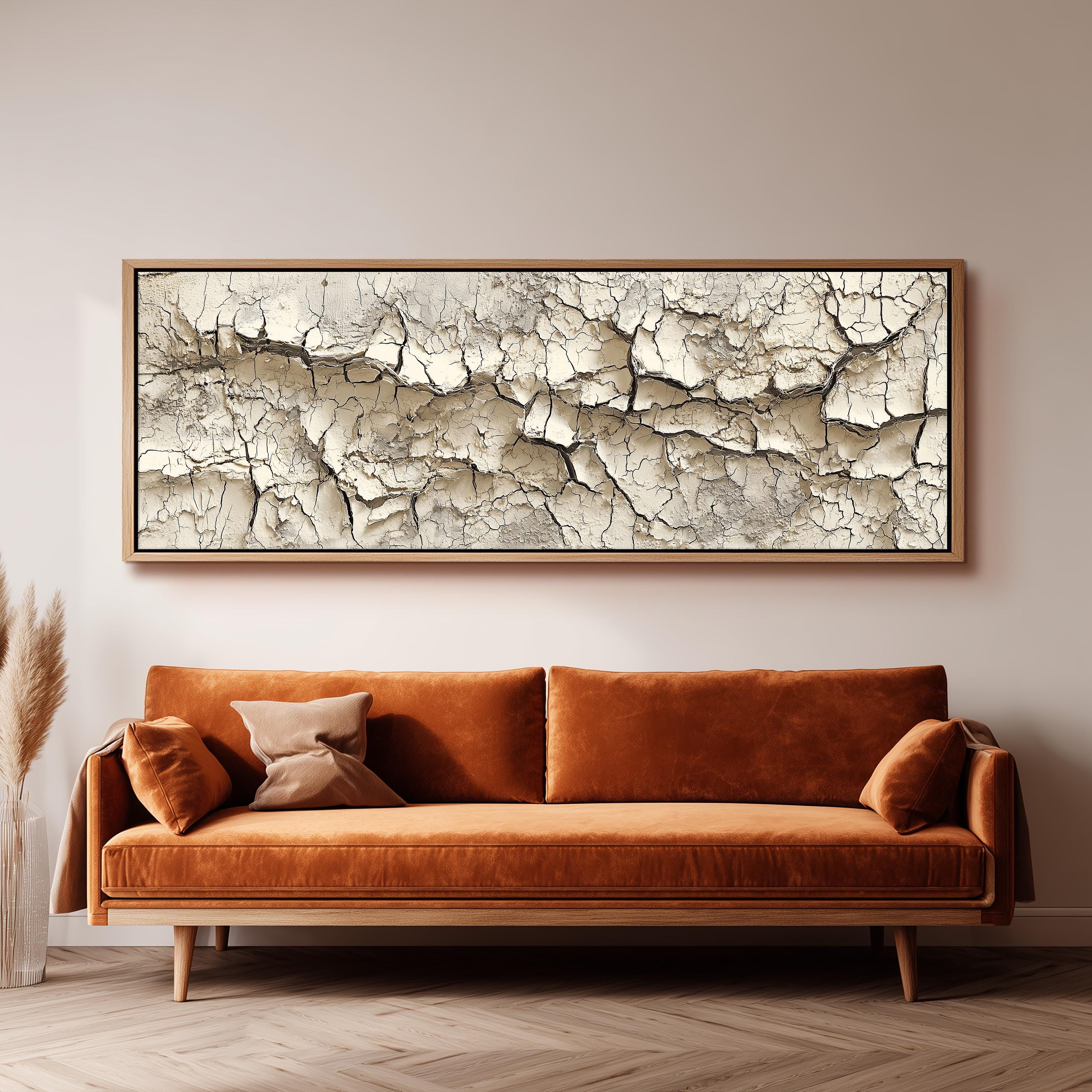 a large, rectangular, and dark brown couch with a wooden frame, positioned in front of a white wall. Above the couch, there is a framed artwork depicting a cracked and weathered surface.