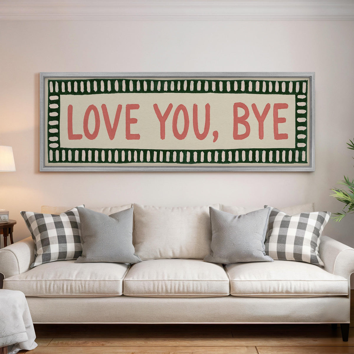 Love you, bye sign with a green border panoramic canvas print above a white sofa in a bright living room
