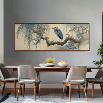 a dining room with a large painting of a blue heron perched on a branch above a wooden table. The table is set with a bowl of fruit and a vase of flowers. The room has gray walls and a gray carpet, creating a calm and elegant atmosphere.
