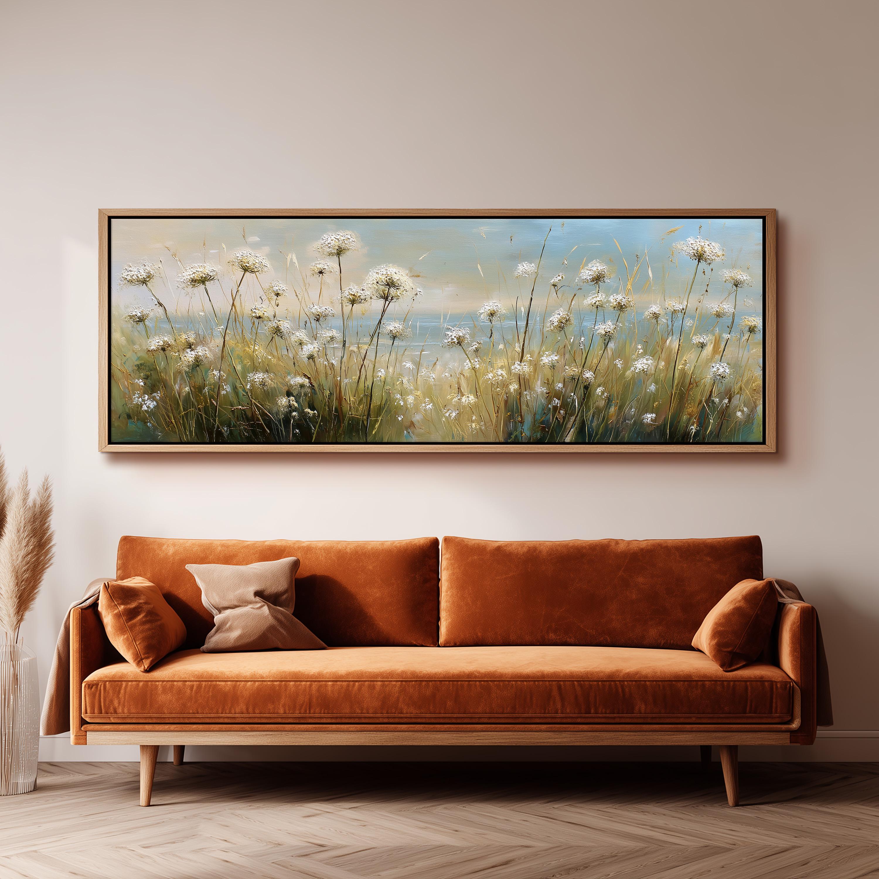 a large painting of a field of flowers hanging on a wall above a brown sofa with orange cushions.