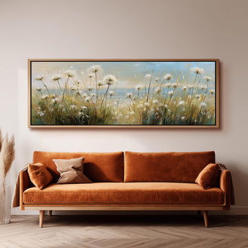 a large painting of a field of flowers hanging on a wall above a brown sofa with orange cushions.