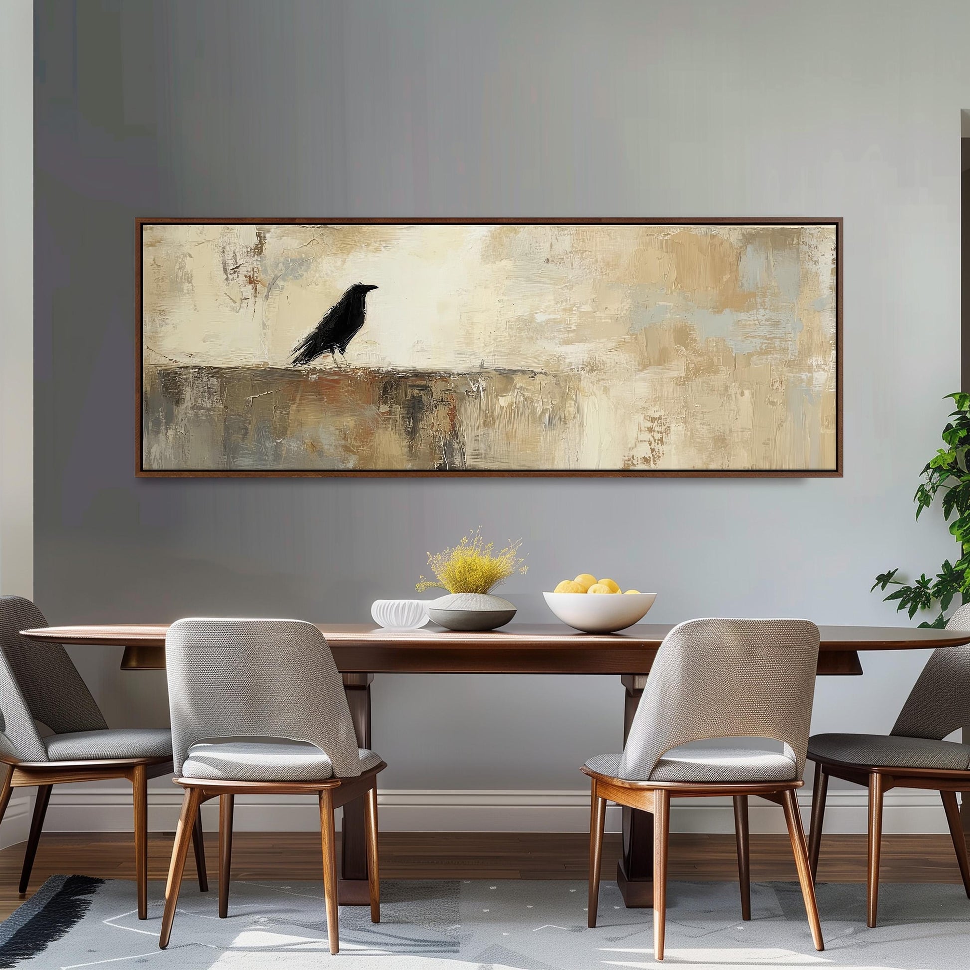 a dining room with a wooden table and four chairs. Above the table, there is a large painting of a black bird. The table is set with a bowl of fruit and a vase of flowers. The room has a neutral color scheme with gray walls and a gray carpet.