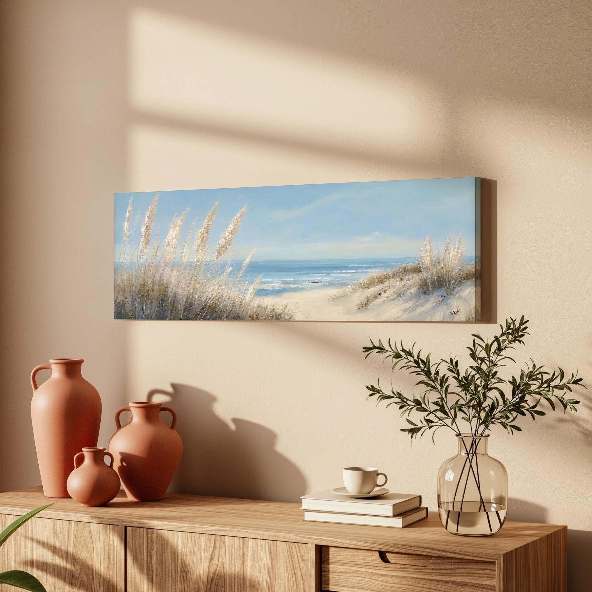 a serene beach scene with a painting of a sandy beach and the ocean, a vase with greenery, and a wooden dresser with books and a coffee cup.