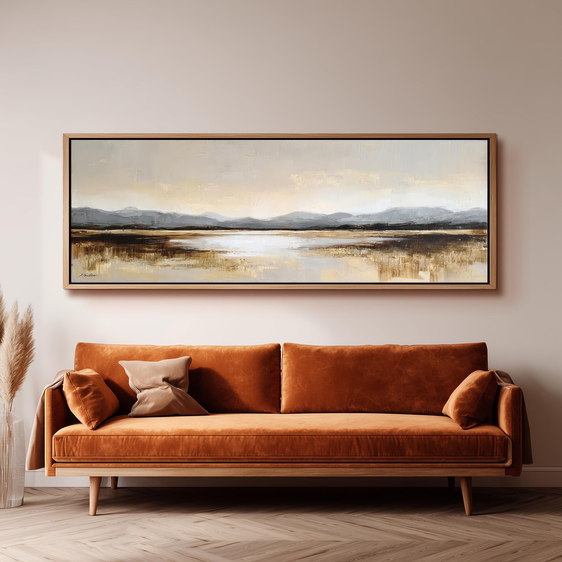 a large landscape painting hanging on a wall above a brown sofa with orange cushions.