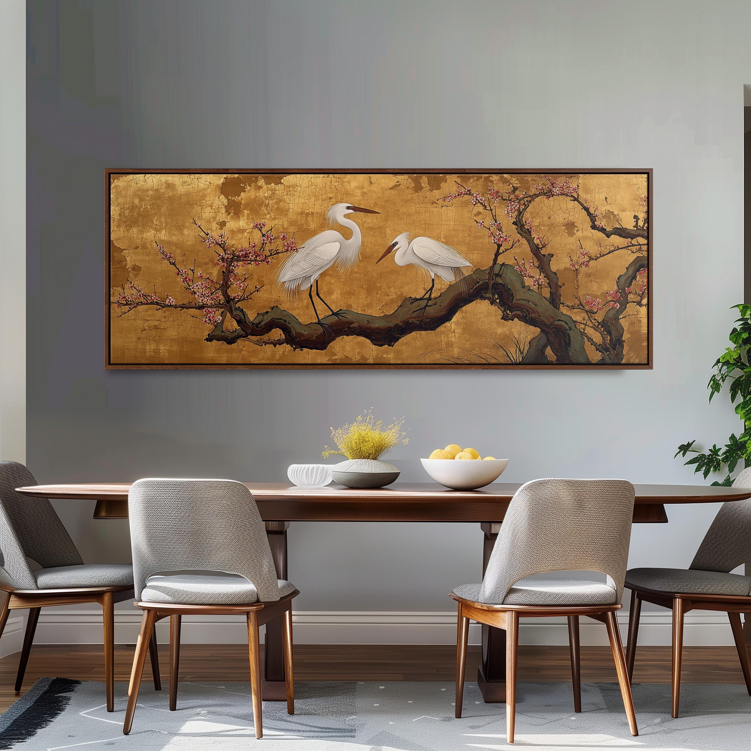 a dining room with a large painting of two white birds perched on a branch above a wooden table. The table is set with a bowl of fruit and a vase of flowers. The room has gray walls and a gray carpet, creating a neutral and elegant atmosphere.