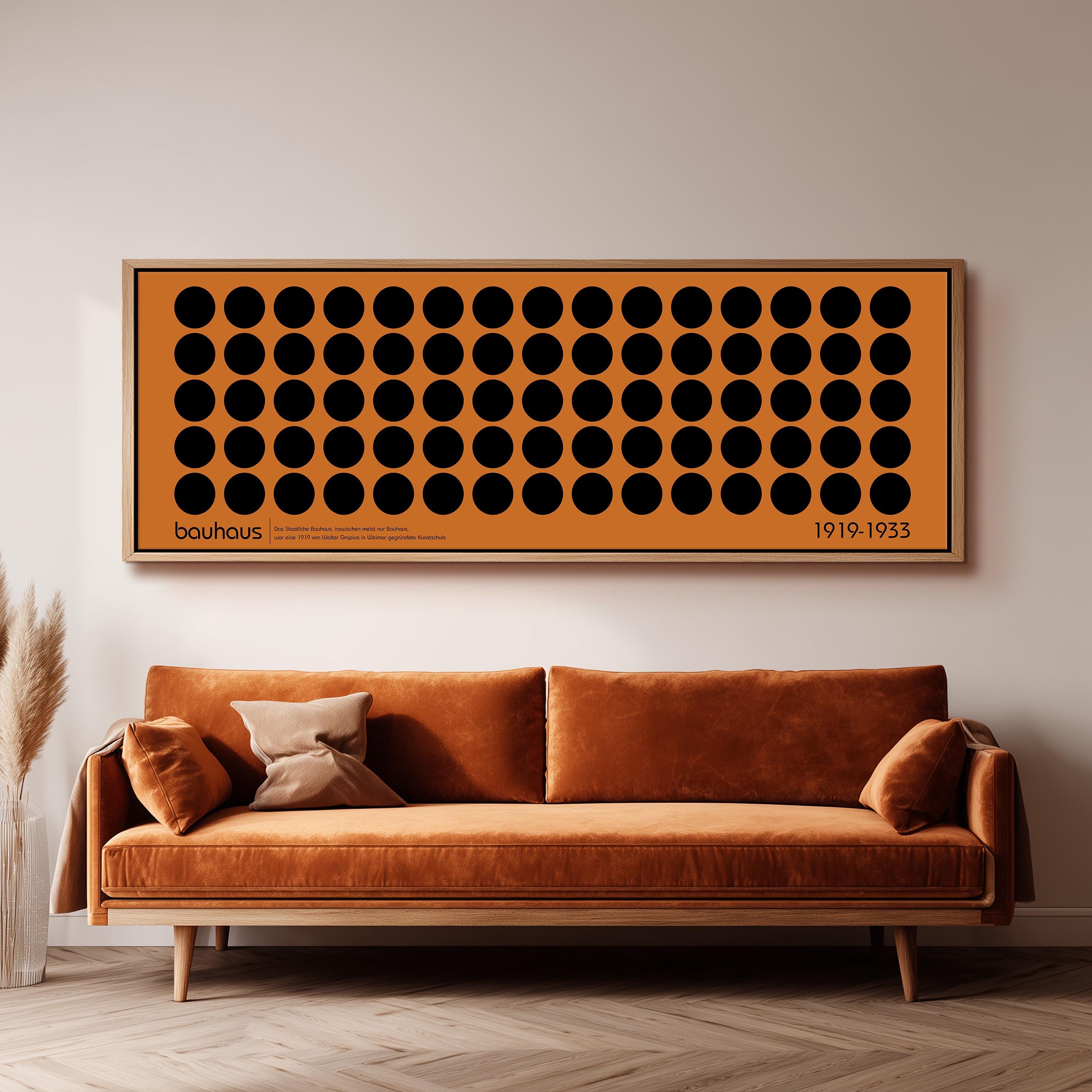 a large orange couch with a brown throw pillow, and a framed artwork with a repeating pattern of black circles is hanging above it on a white wall.