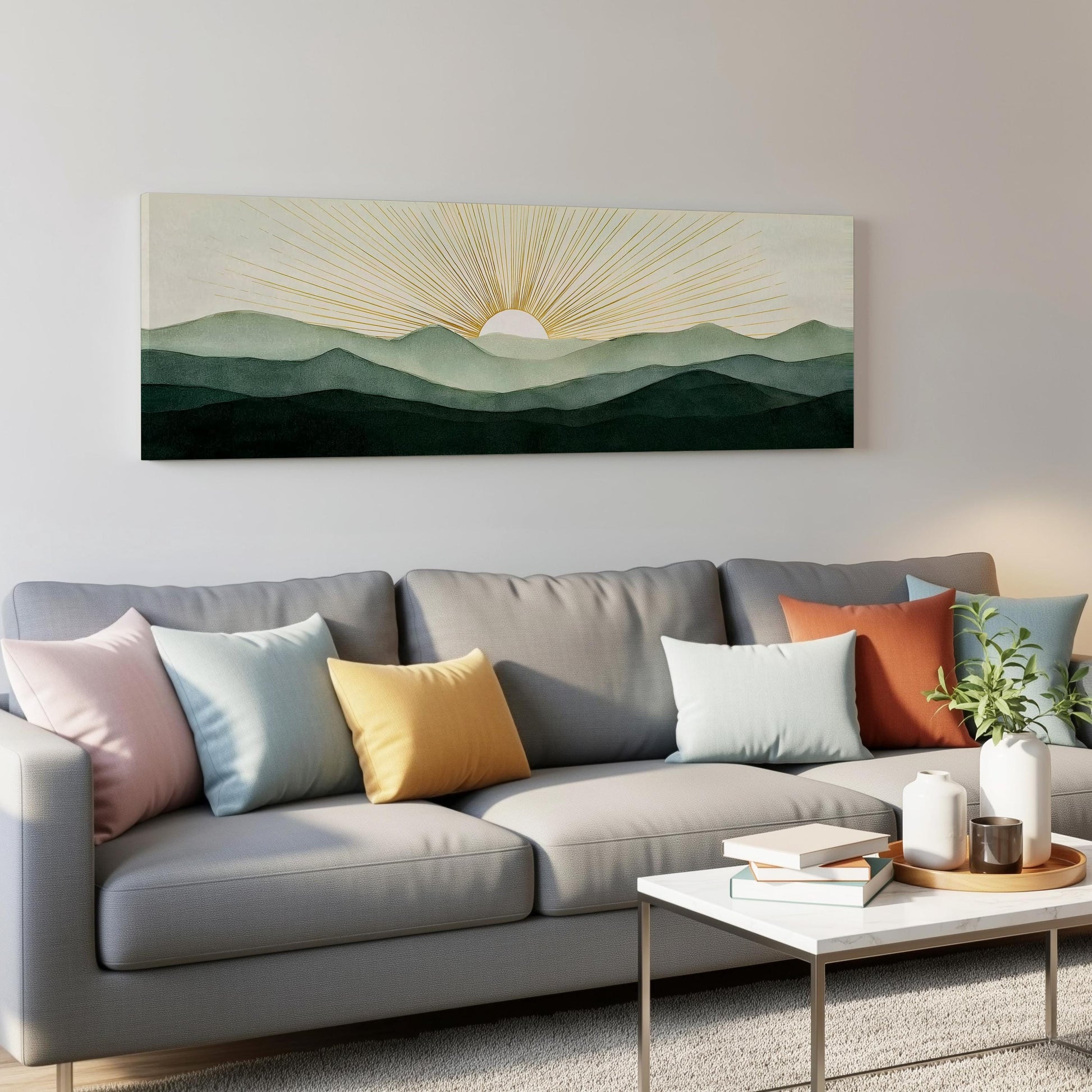 a living room with a gray sofa adorned with colorful throw pillows, a coffee table with books and a plant, and a large wall art depicting a sun rising over a mountain range.
