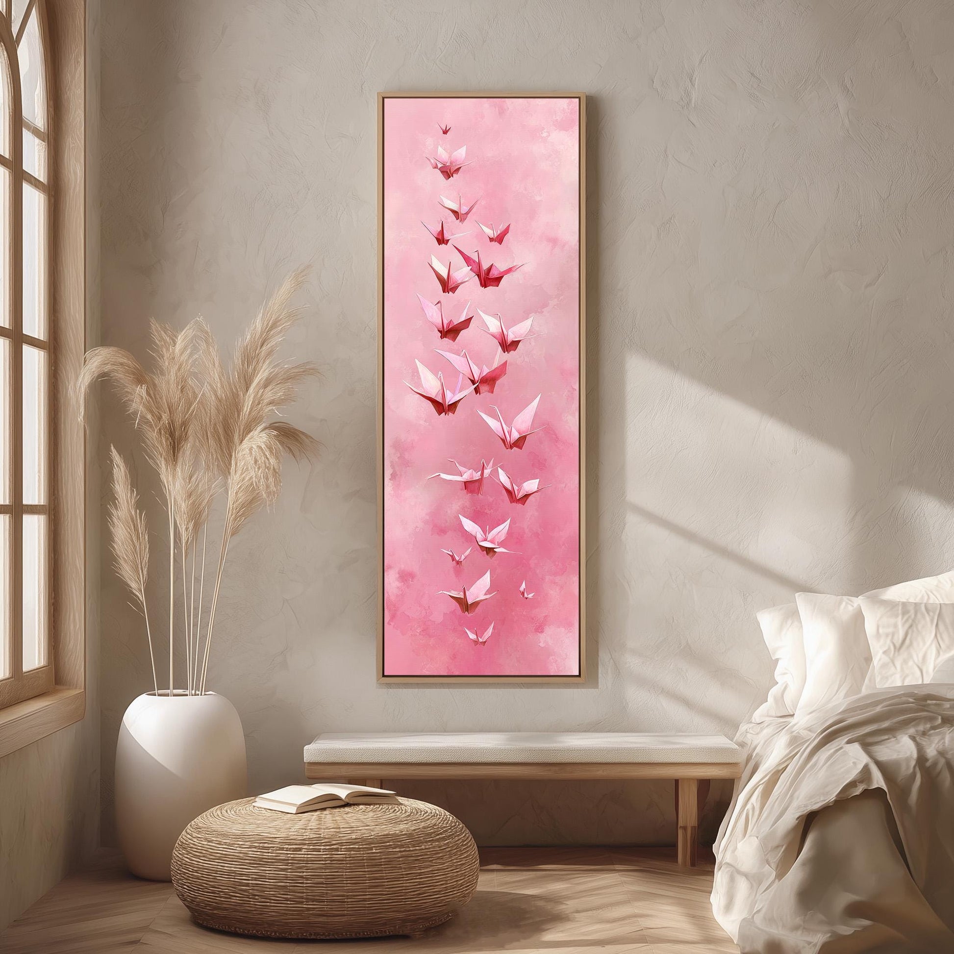 a large, framed painting of pink butterflies hanging on a wall in a bedroom. The painting is surrounded by a white vase filled with tall, light-colored reeds, and a white bench is positioned next to the painting. The room has a minimalist and serene atmosphere, with a bed and a window providing natural light.