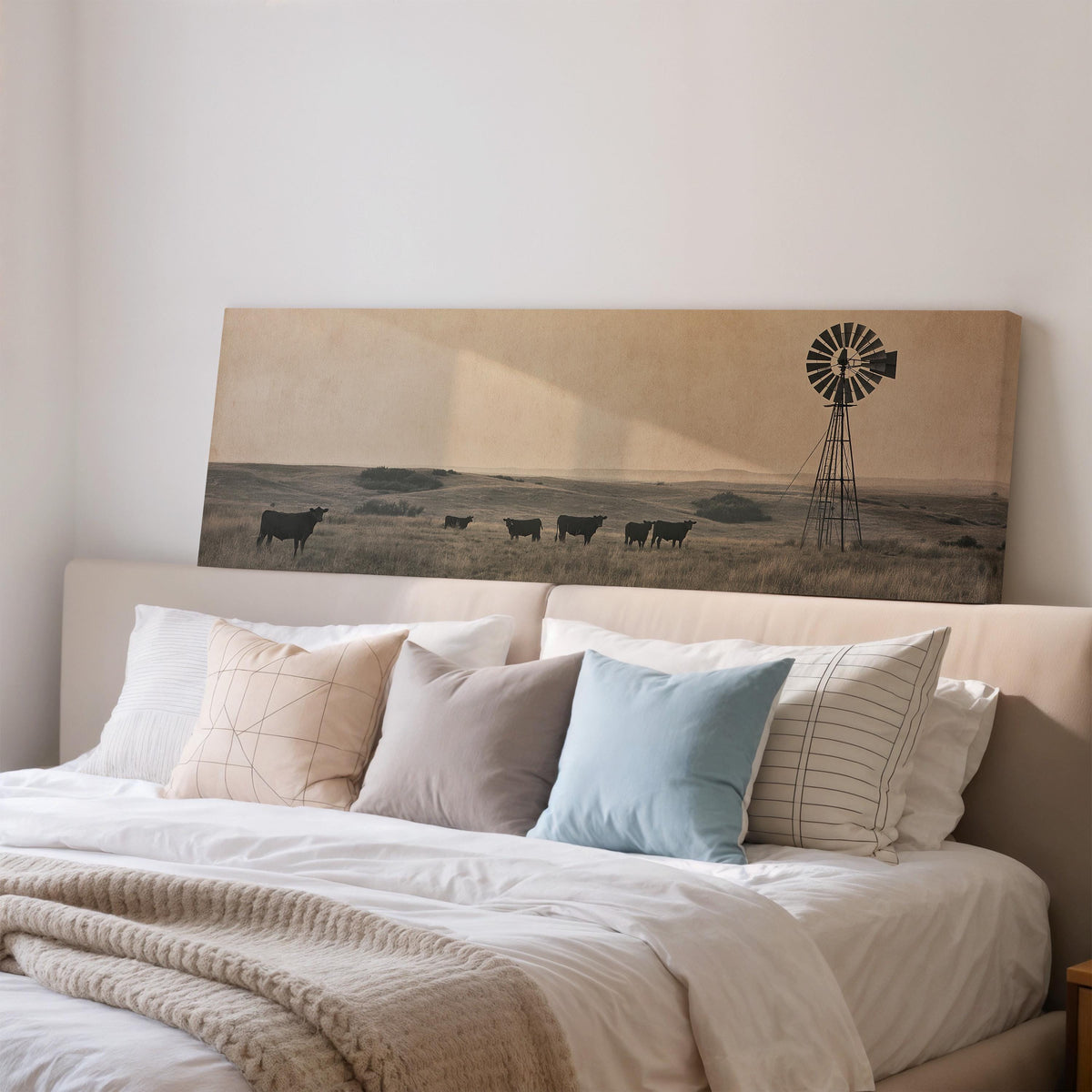 Black cattle grazing by a windmill on the prairie wide panoramic canvas print above a bed in a bedroom