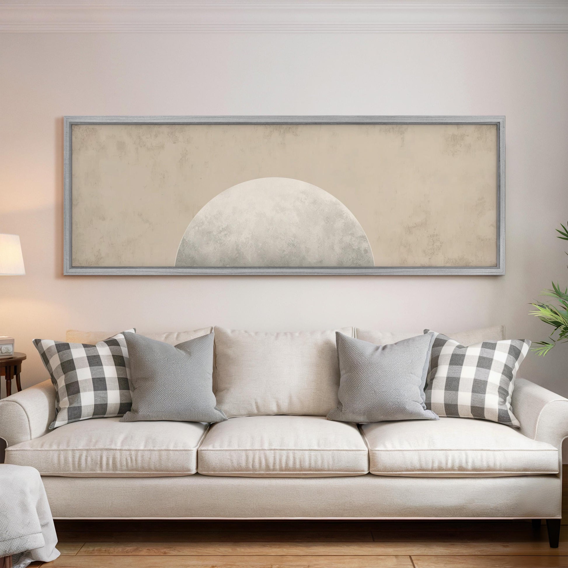 a living room with a white sofa adorned with gray and white plaid throw pillows. Above the sofa, there is a large framed artwork depicting a moon-like shape.