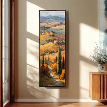 a large framed painting of a picturesque countryside landscape, with rolling hills, trees, and a winding path. The painting is hung on a wall in a room with a window, creating a serene and peaceful atmosphere.