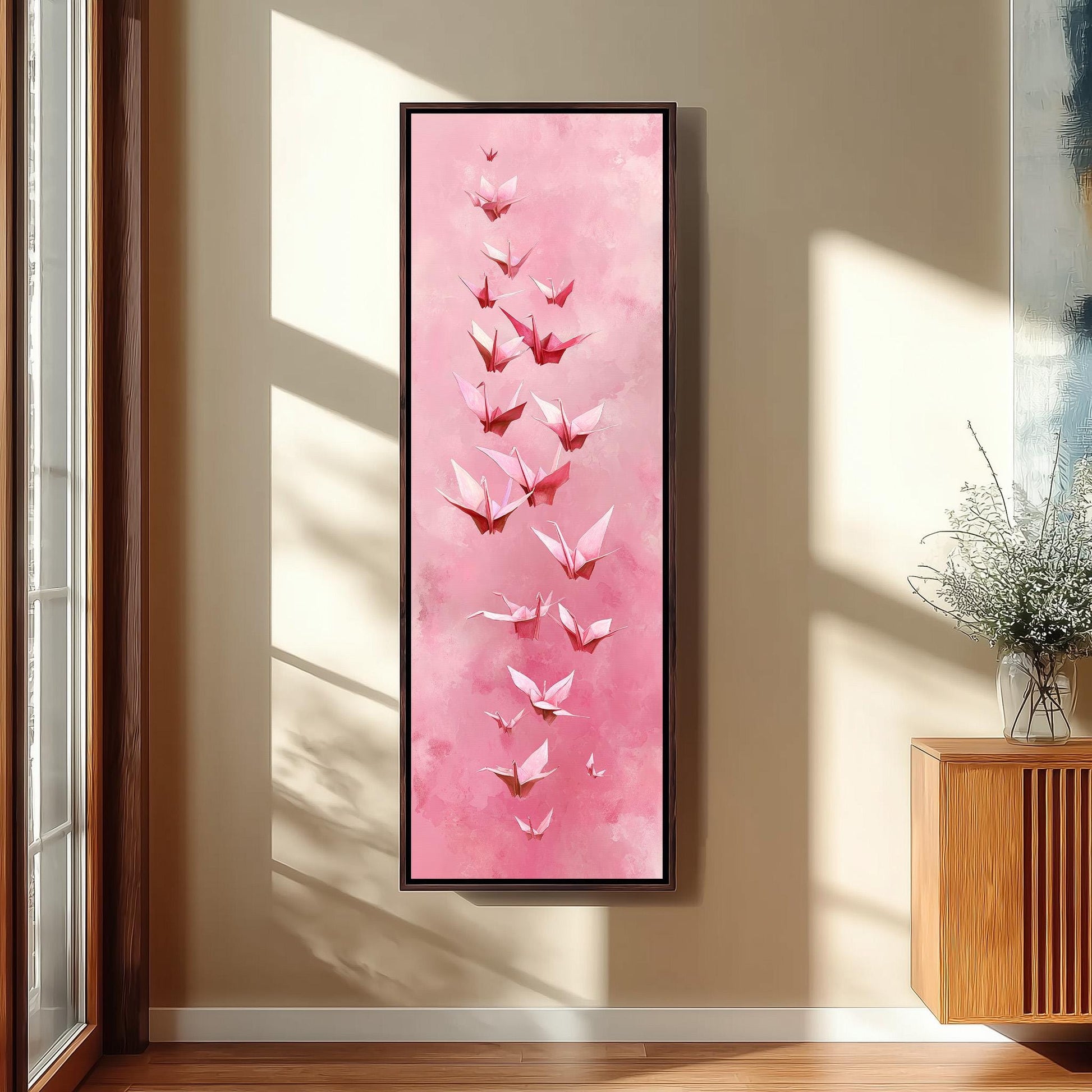 a large framed painting of pink origami butterflies hanging on a wall in a room with a wooden cabinet and a vase of flowers.