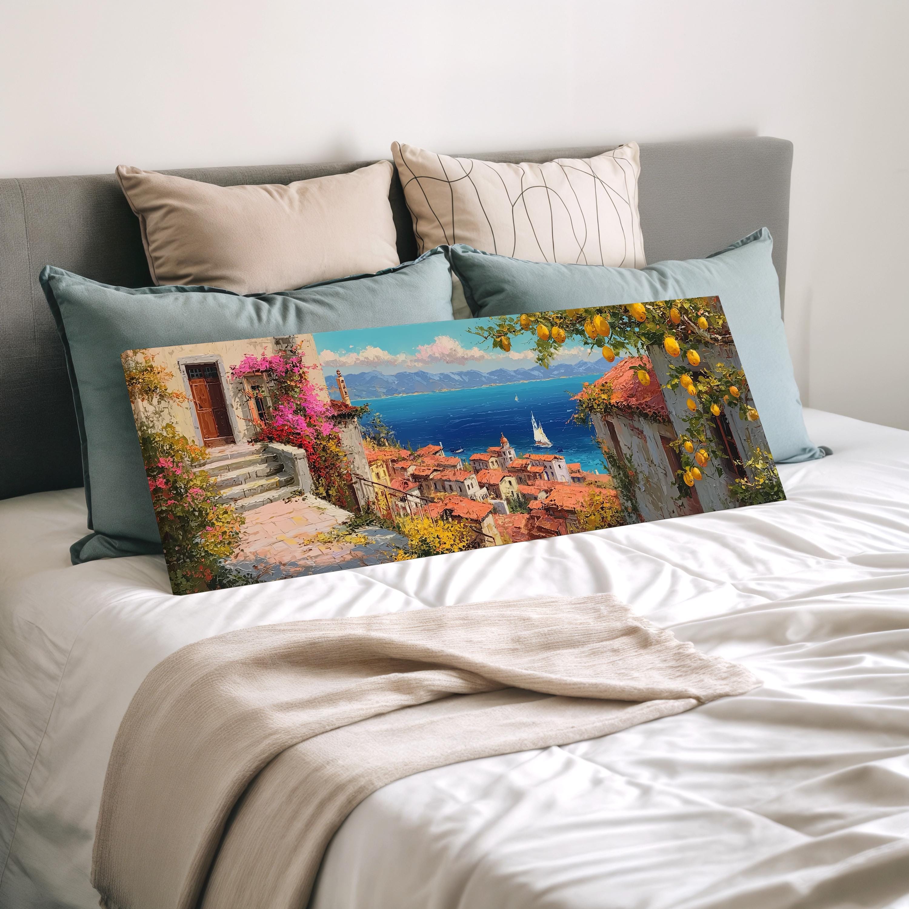 a large, colorful painting of a coastal town with a boat in the distance, displayed on a bed with pillows.