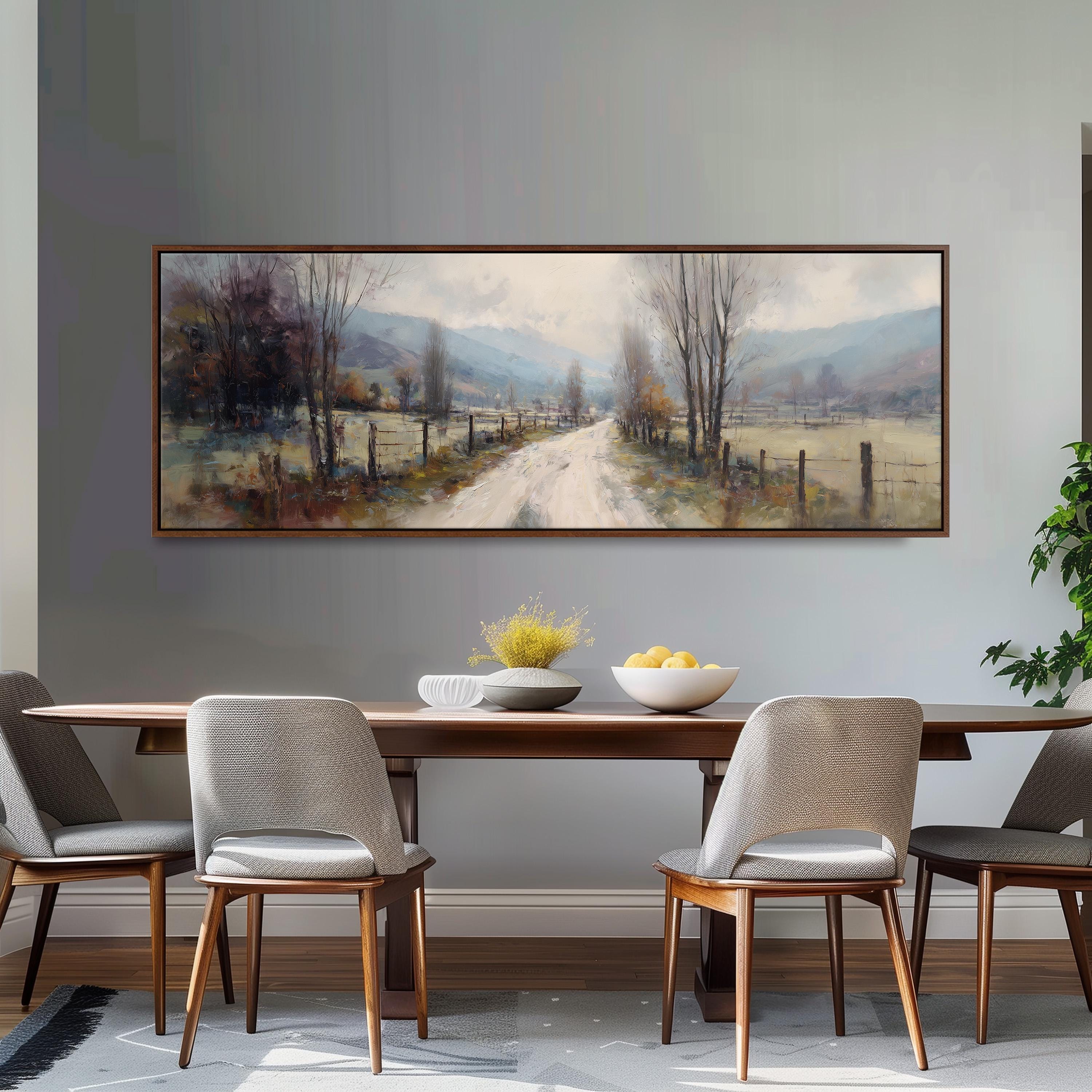 a large painting of a countryside road with trees and a bowl of fruit on a table in front of it.