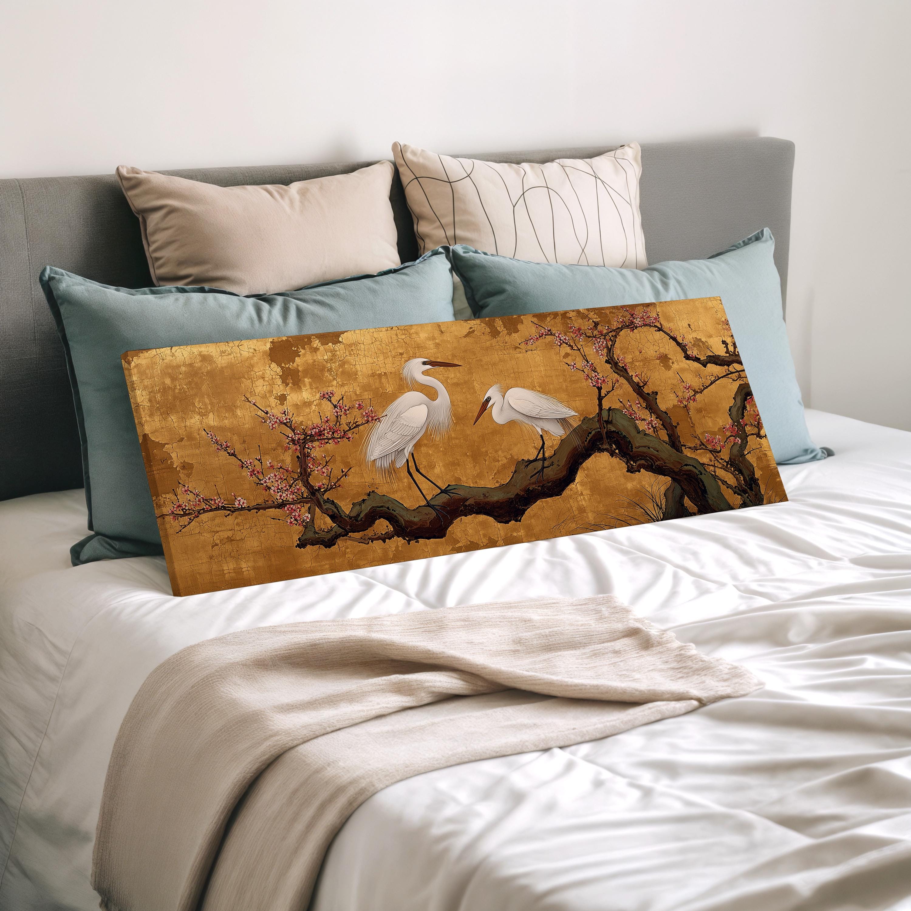 a large painting of two white birds perched on a branch with pink flowers, displayed on a bed with a white comforter and pillows.