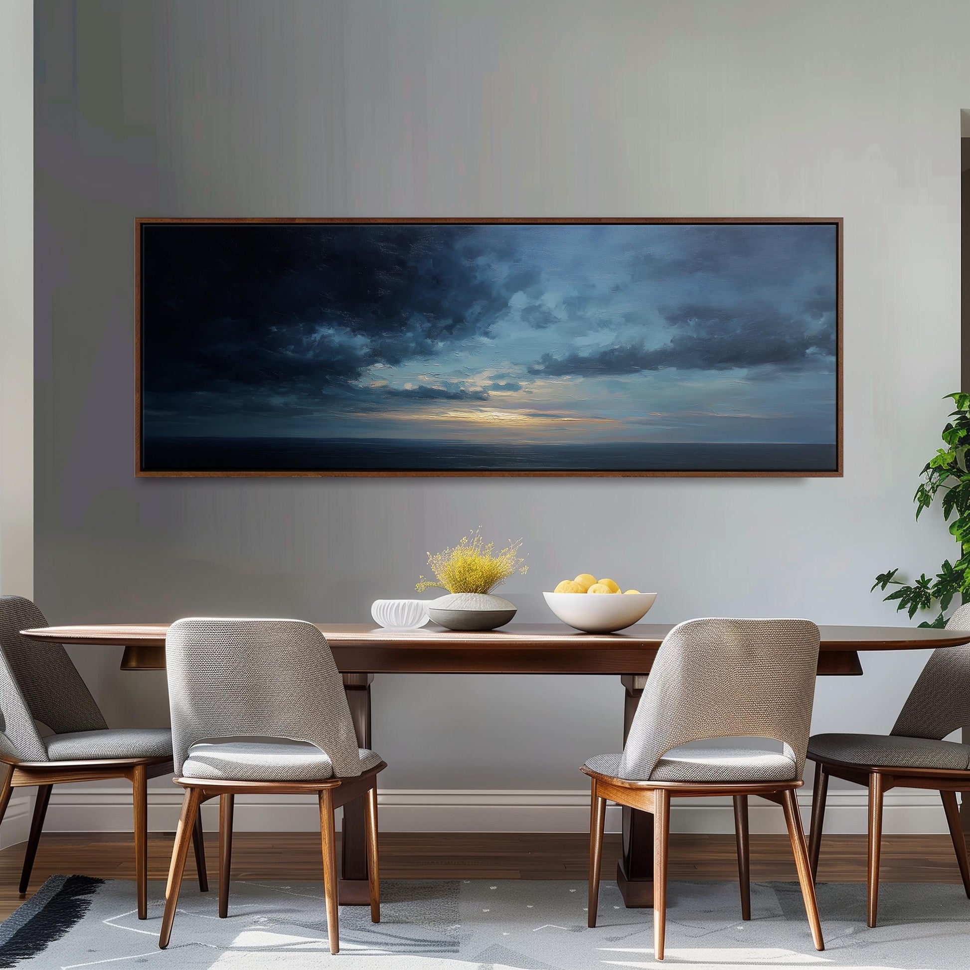 a dining room with a large painting of a stormy sky hanging on the wall above a wooden dining table with four chairs. The table is set with a bowl of fruit and a vase of flowers, creating a cozy and inviting atmosphere.