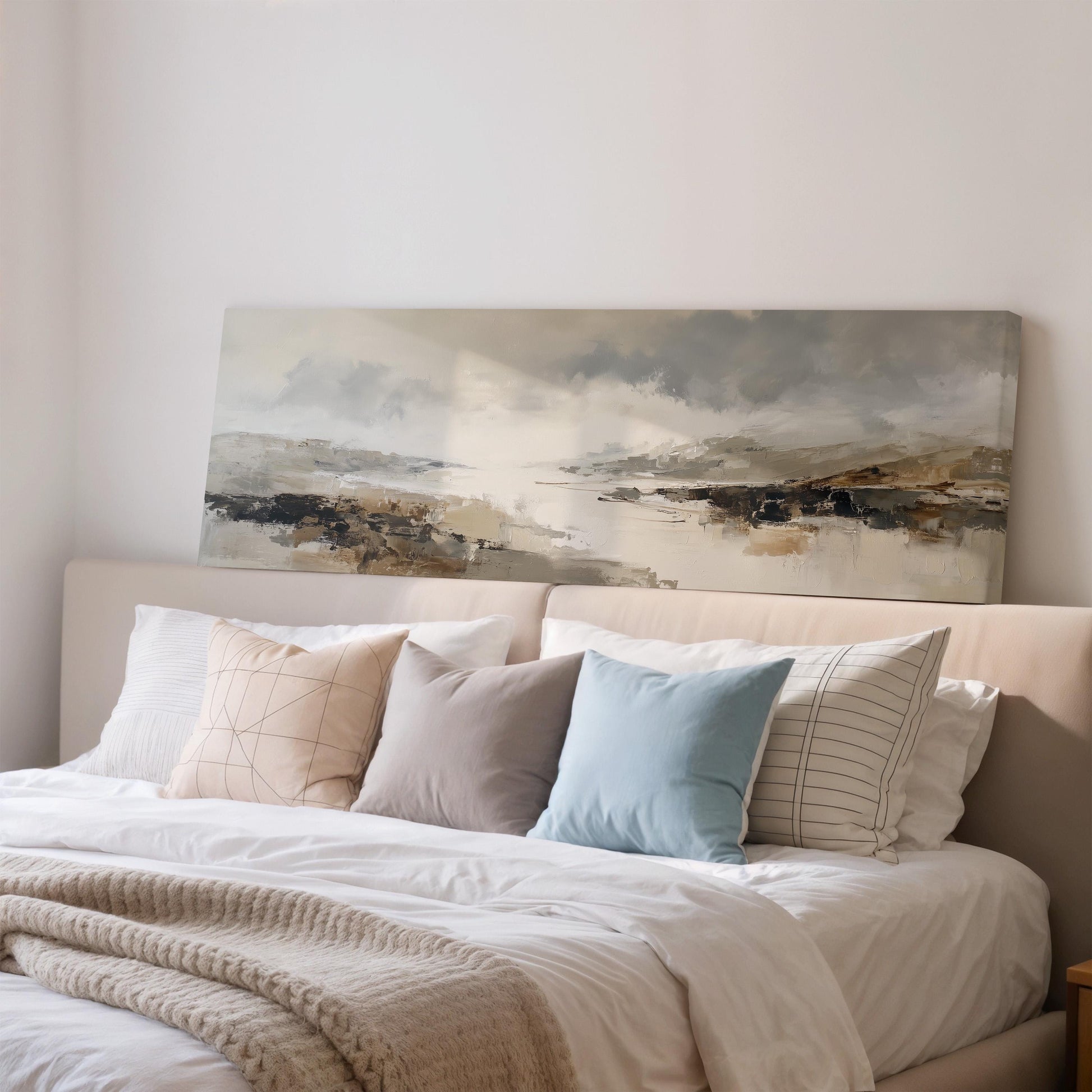 a cozy bedroom with a large bed adorned with a variety of pillows and a blanket. Above the bed, there is a painting of a landscape, adding an artistic touch to the room's decor.