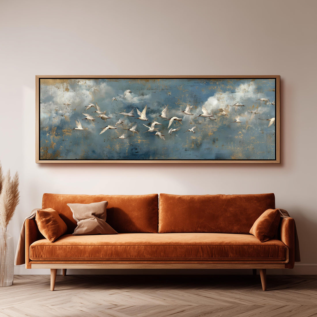a large painting of a flock of birds flying over a cloudy sky, hanging on a wall above a white sofa with gray and white patterned pillows.