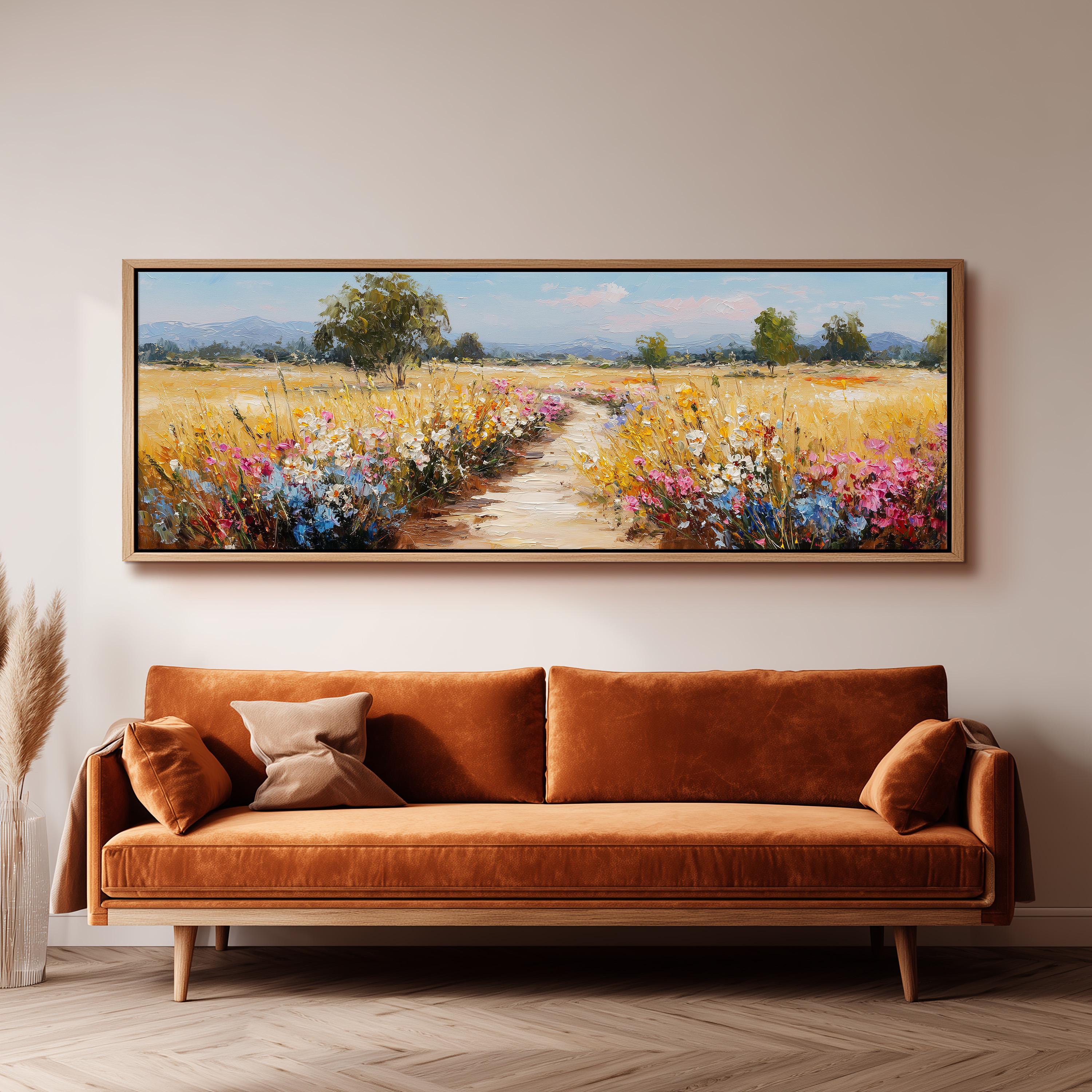 a large, framed painting of a field with flowers hanging on a wall above a brown sofa.