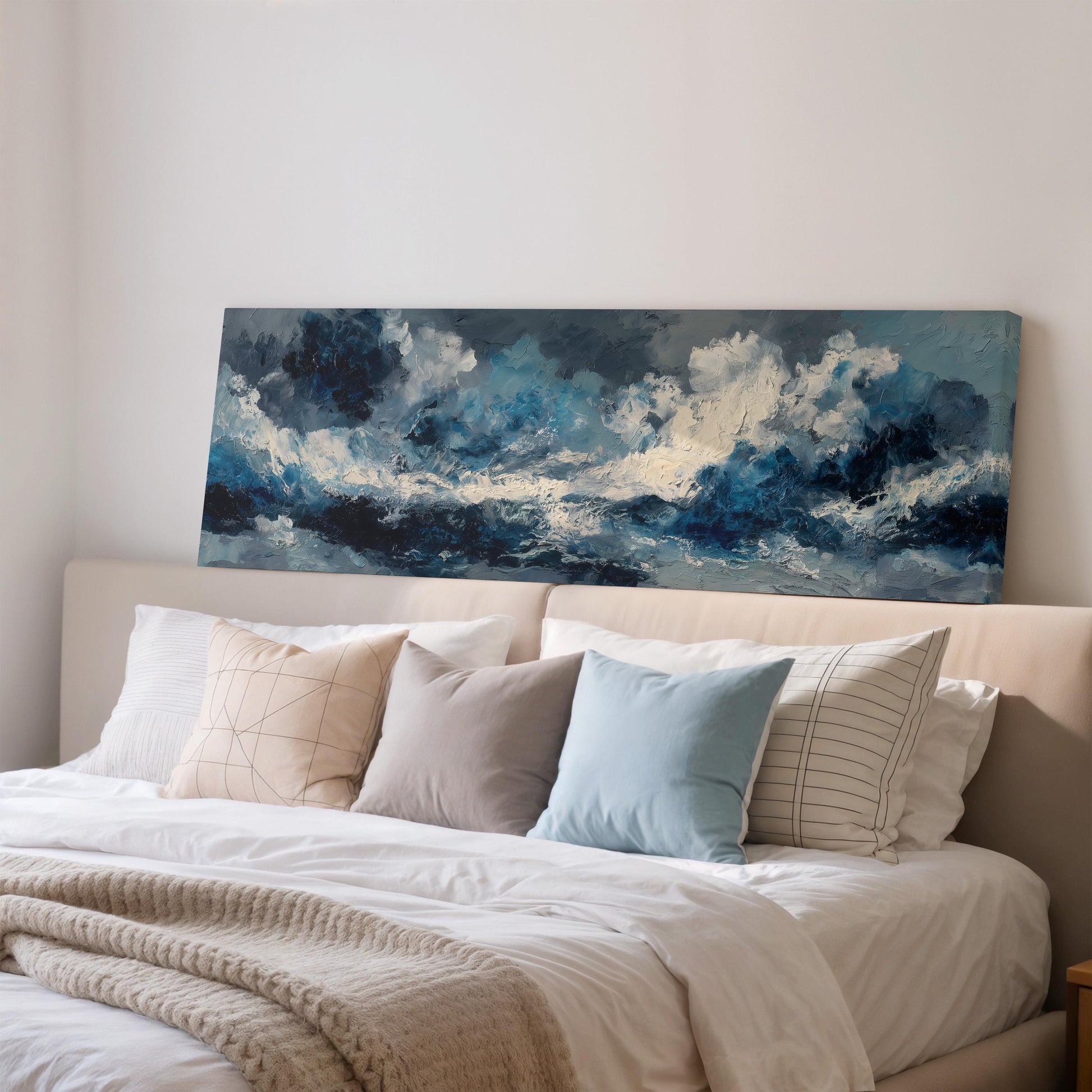 a large painting of a stormy ocean scene hanging on a wall above a bed with white pillows and a gray blanket.