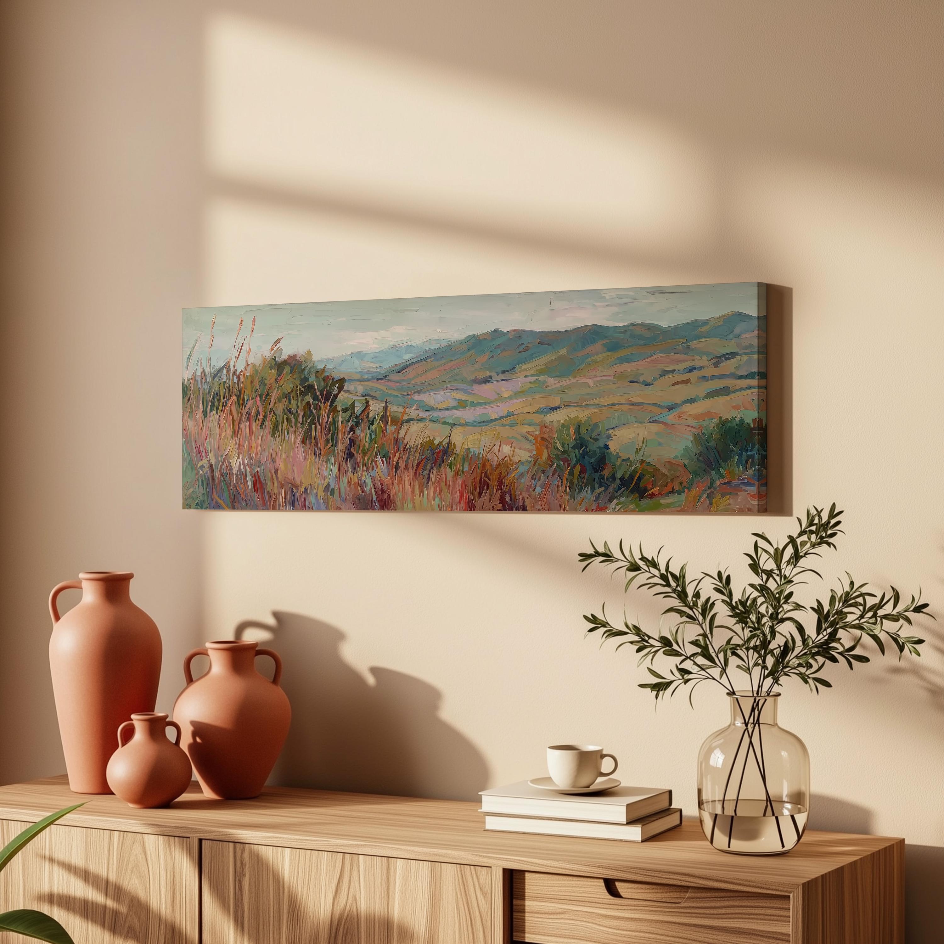 a wooden cabinet with a painting of a landscape hanging on the wall above it. The cabinet also has three orange vases and a glass vase with greenery, as well as a stack of books and a cup on the surface.