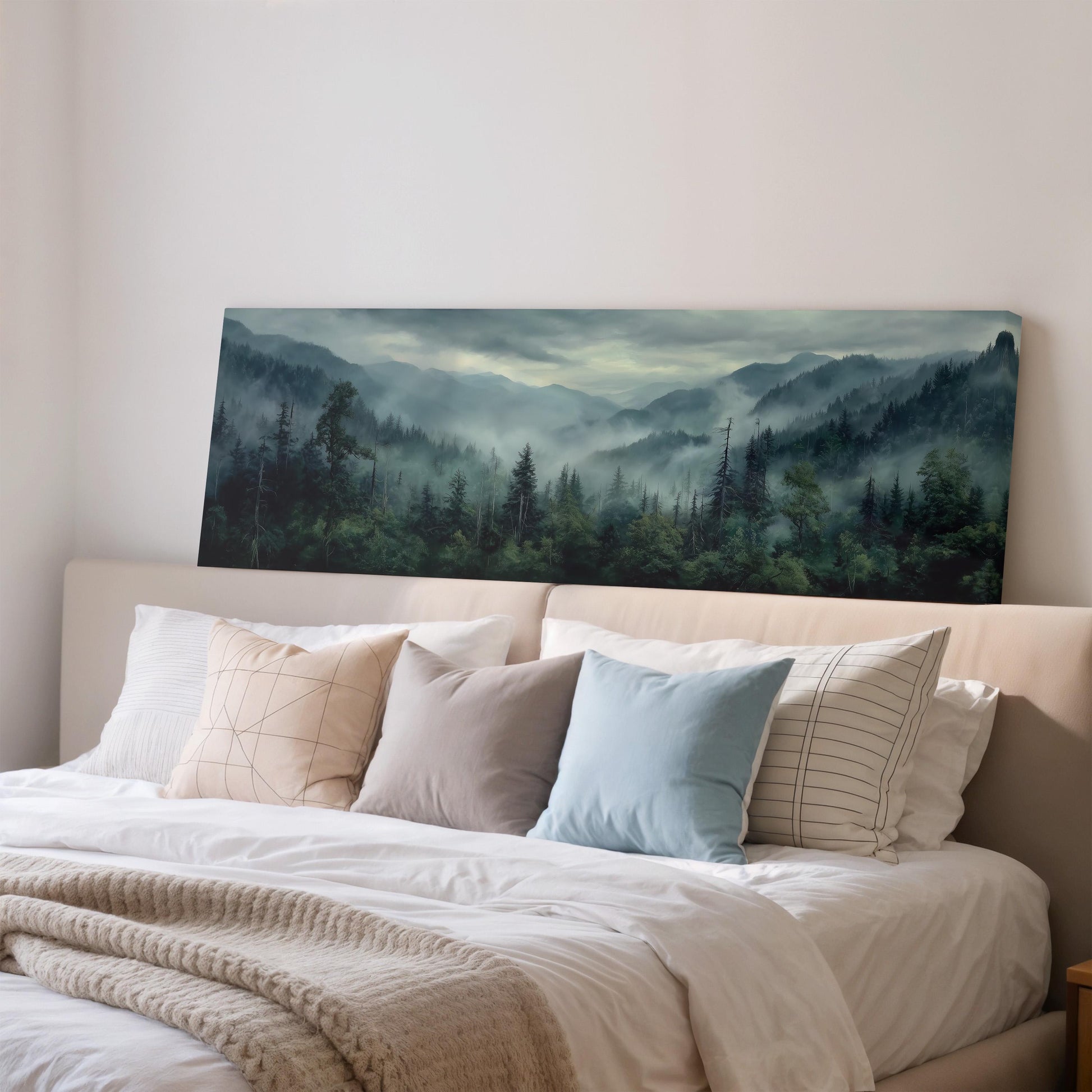 a large landscape painting hanging on a wall above a bed with white pillows and a gray blanket.