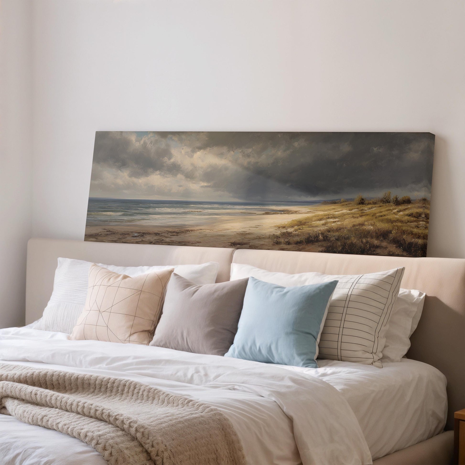 a large painting of a beach scene hanging on a wall above a bed with white bedding and various pillows.