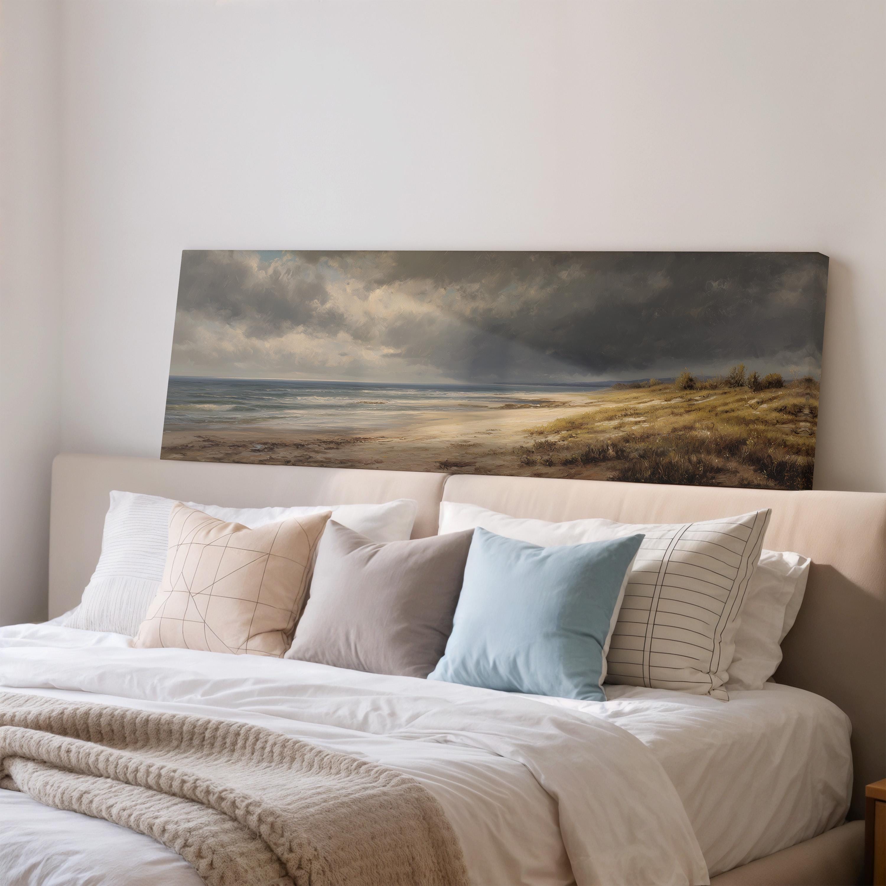 a large painting of a beach scene hanging on a wall above a bed with white bedding and various pillows.