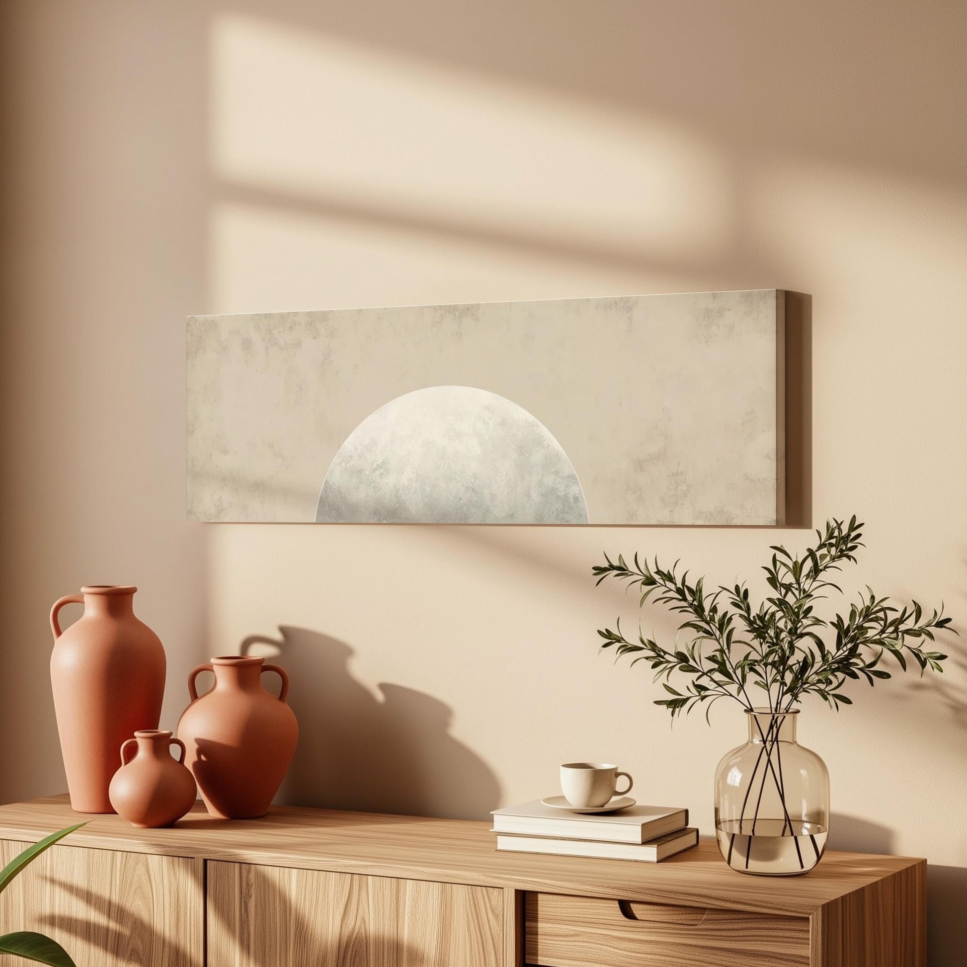 a wooden cabinet with a vase of greenery, a coffee cup, and a stack of books on top. The cabinet is set against a beige wall, and there is a painting hanging above it.